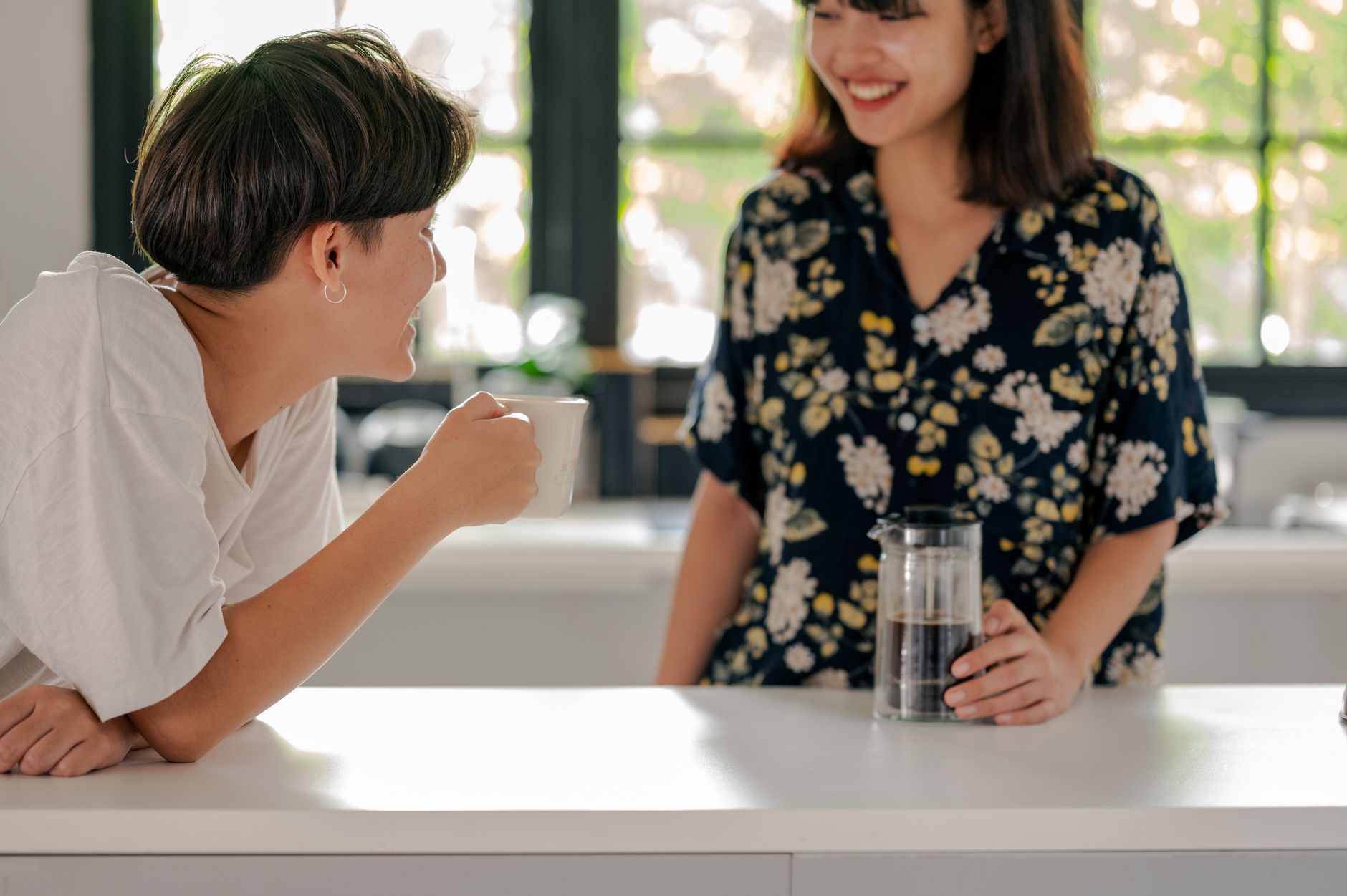 Two friends enjoying coffee together in a bright, modern kitchen setting.