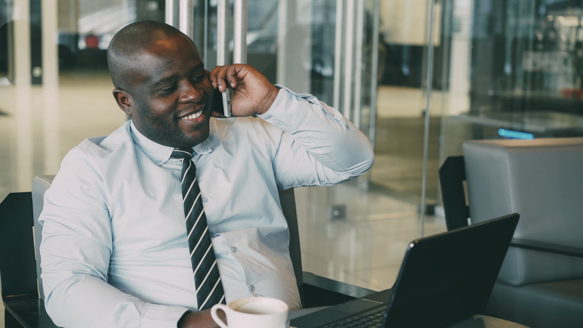 Smiling businessman talking on the phone while working on laptop in modern office.