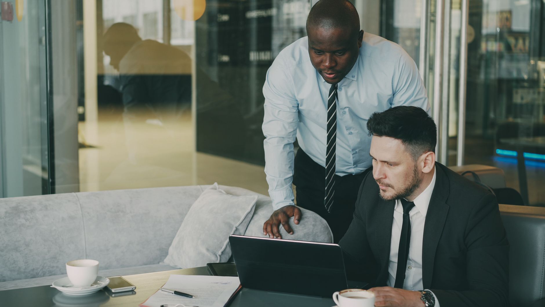 Two businessmen discussing work over a laptop in a contemporary office setting.