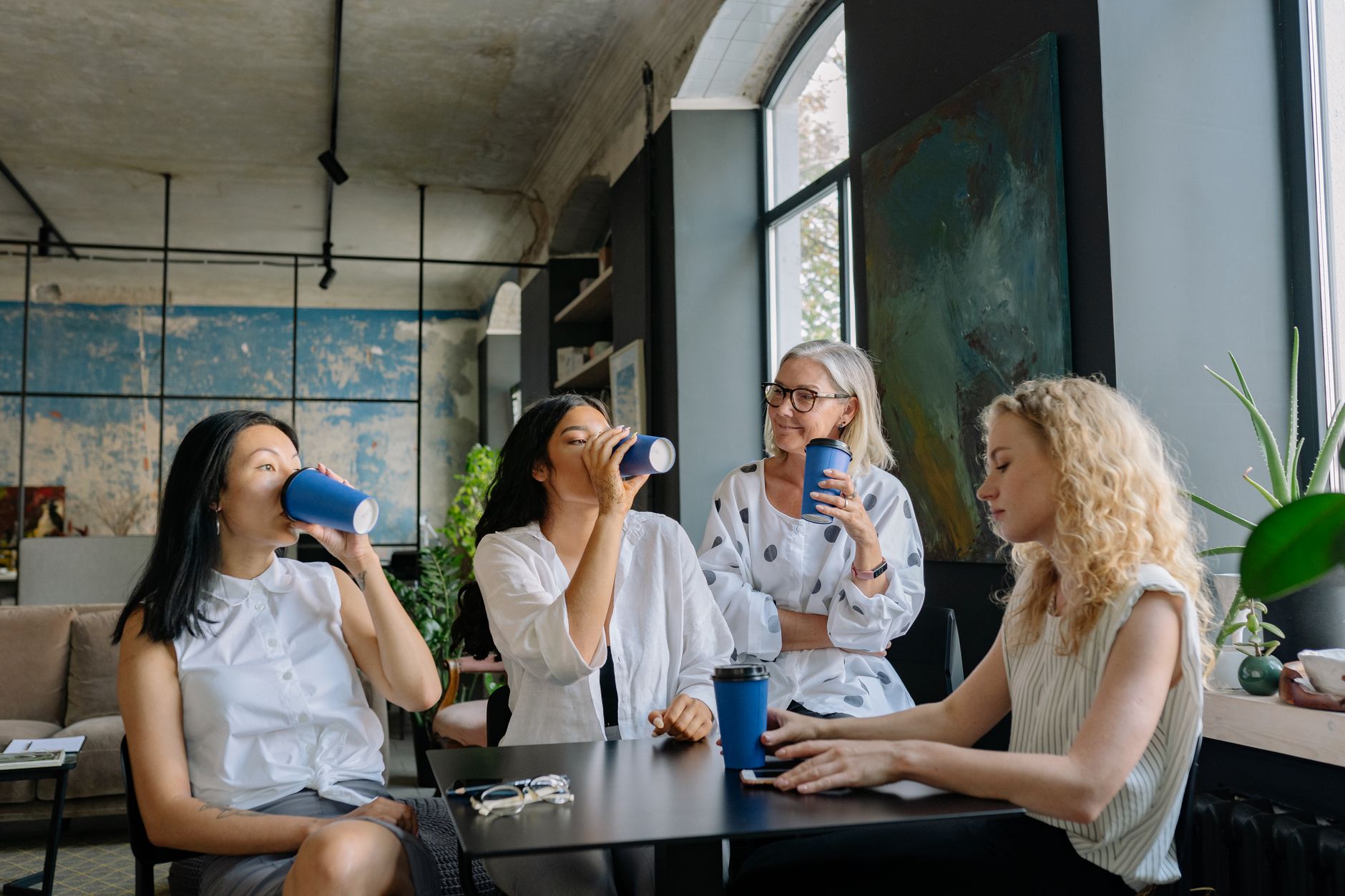 Group of diverse women sharing a coffee break in a modern office setting, fostering teamwork and collaboration.