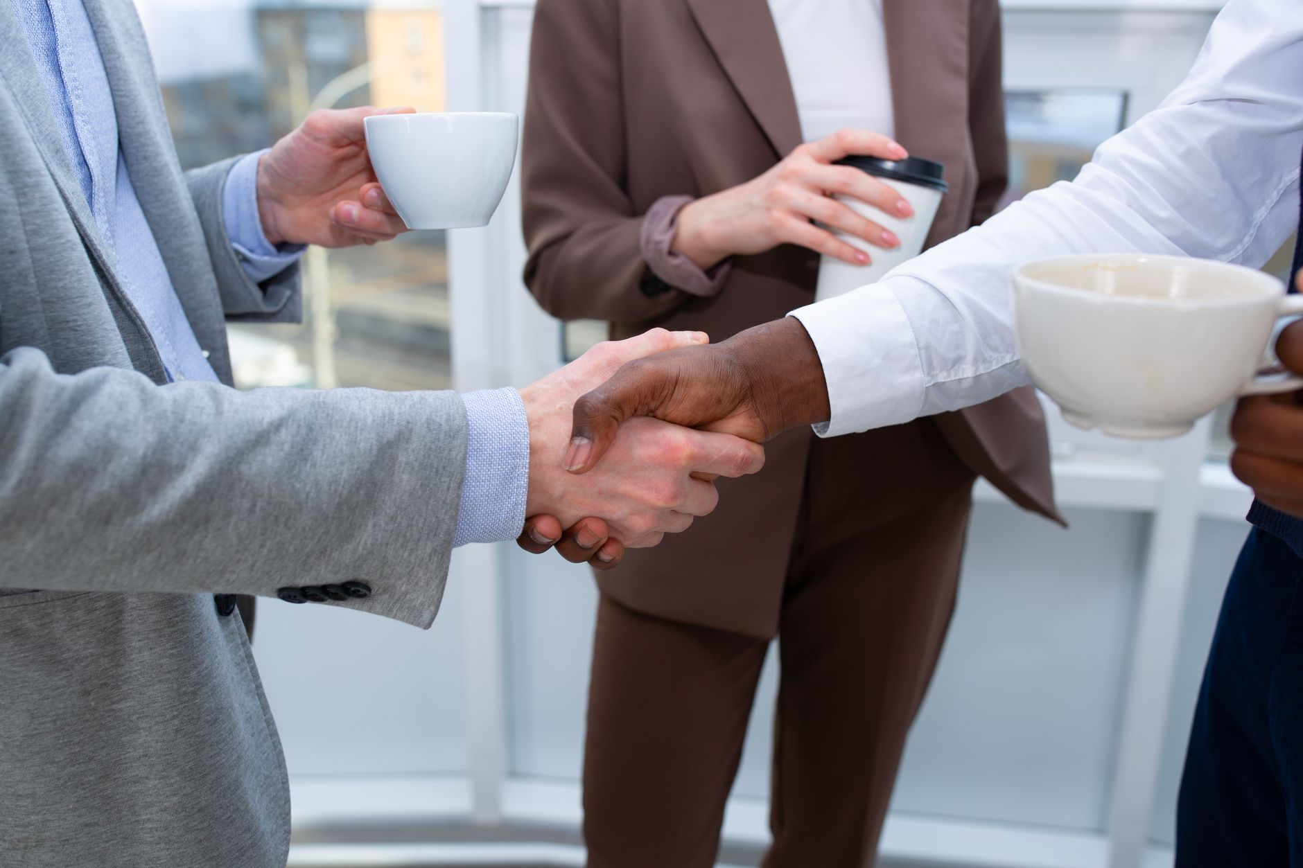 A professional handshake between colleagues holding coffee cups, symbolizing collaboration.