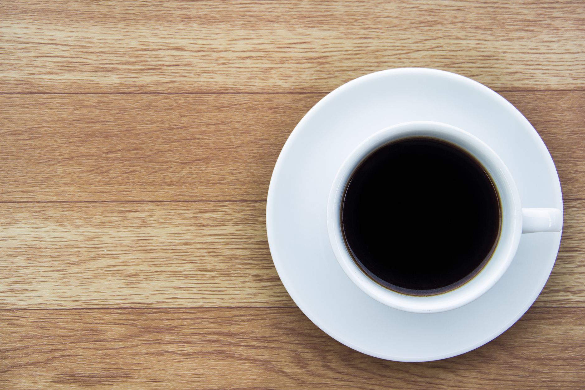 Overhead shot of black coffee in white cup on a wooden surface, ideal for food and drink themes.