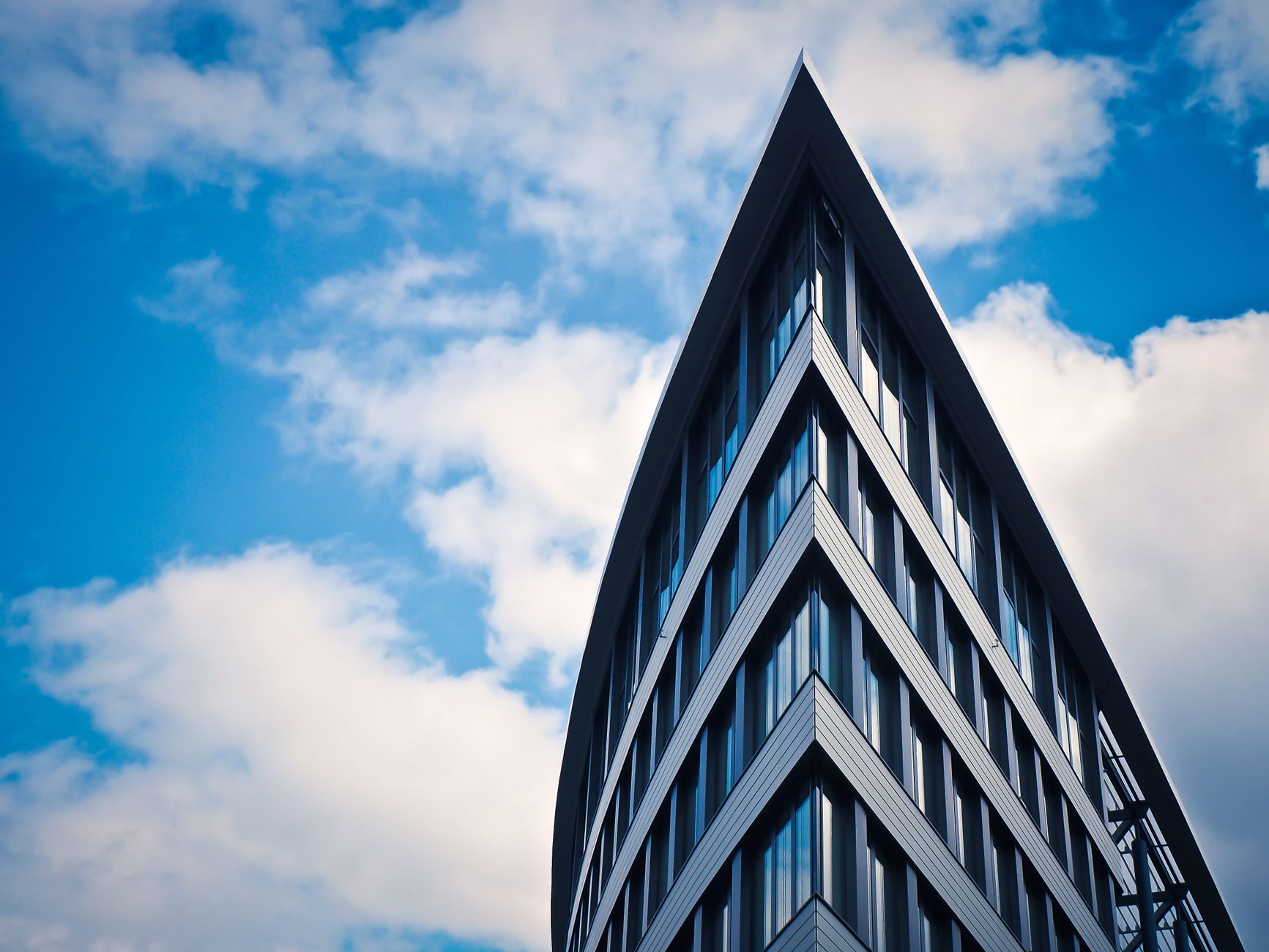 Futuristic skyscraper with glass facade set against a vibrant blue sky with clouds.