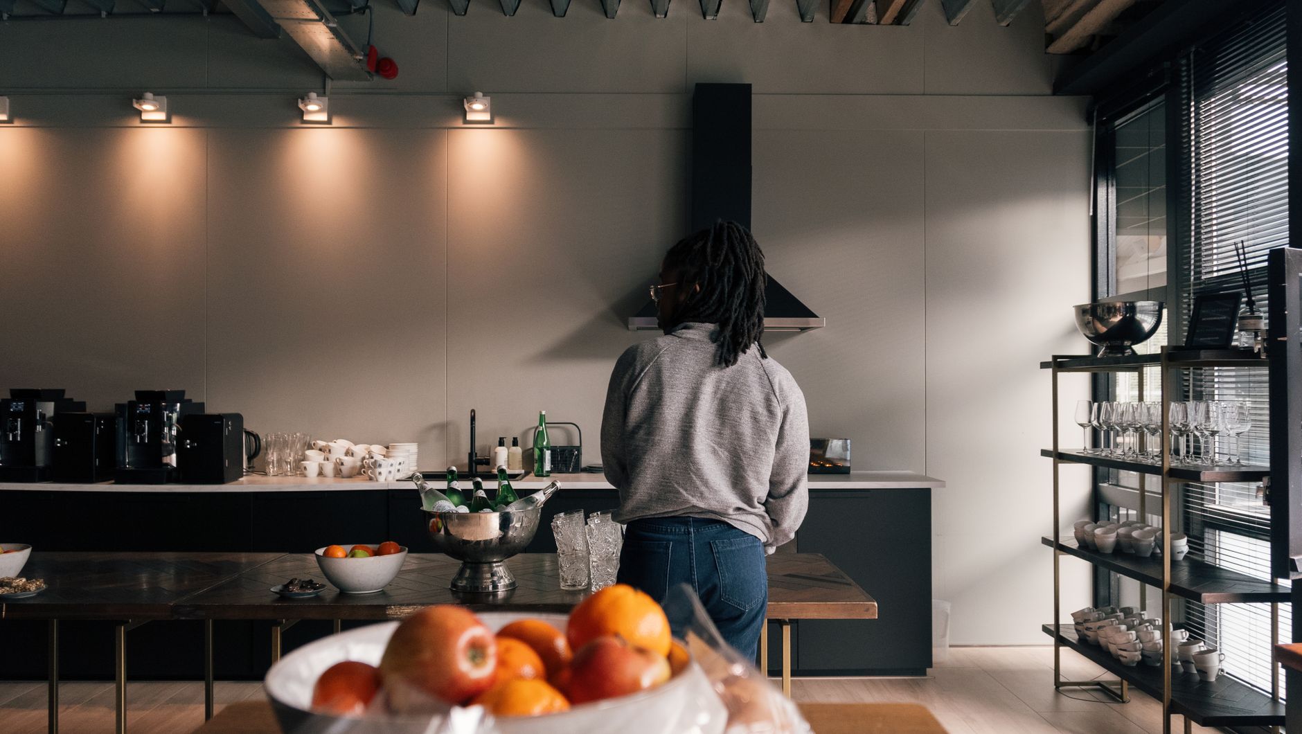 Contemporary kitchen with a person preparing food, featuring a fruit bowl and kitchenware.