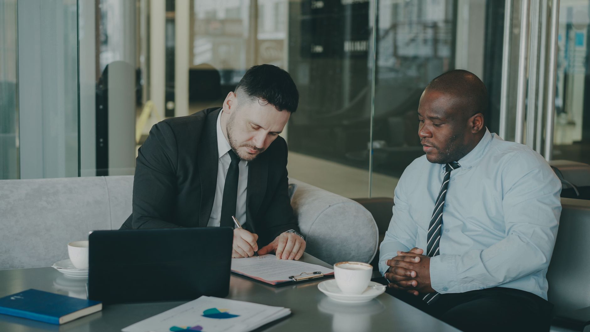 Two businessmen reviewing documents in a stylish office setting with coffee.