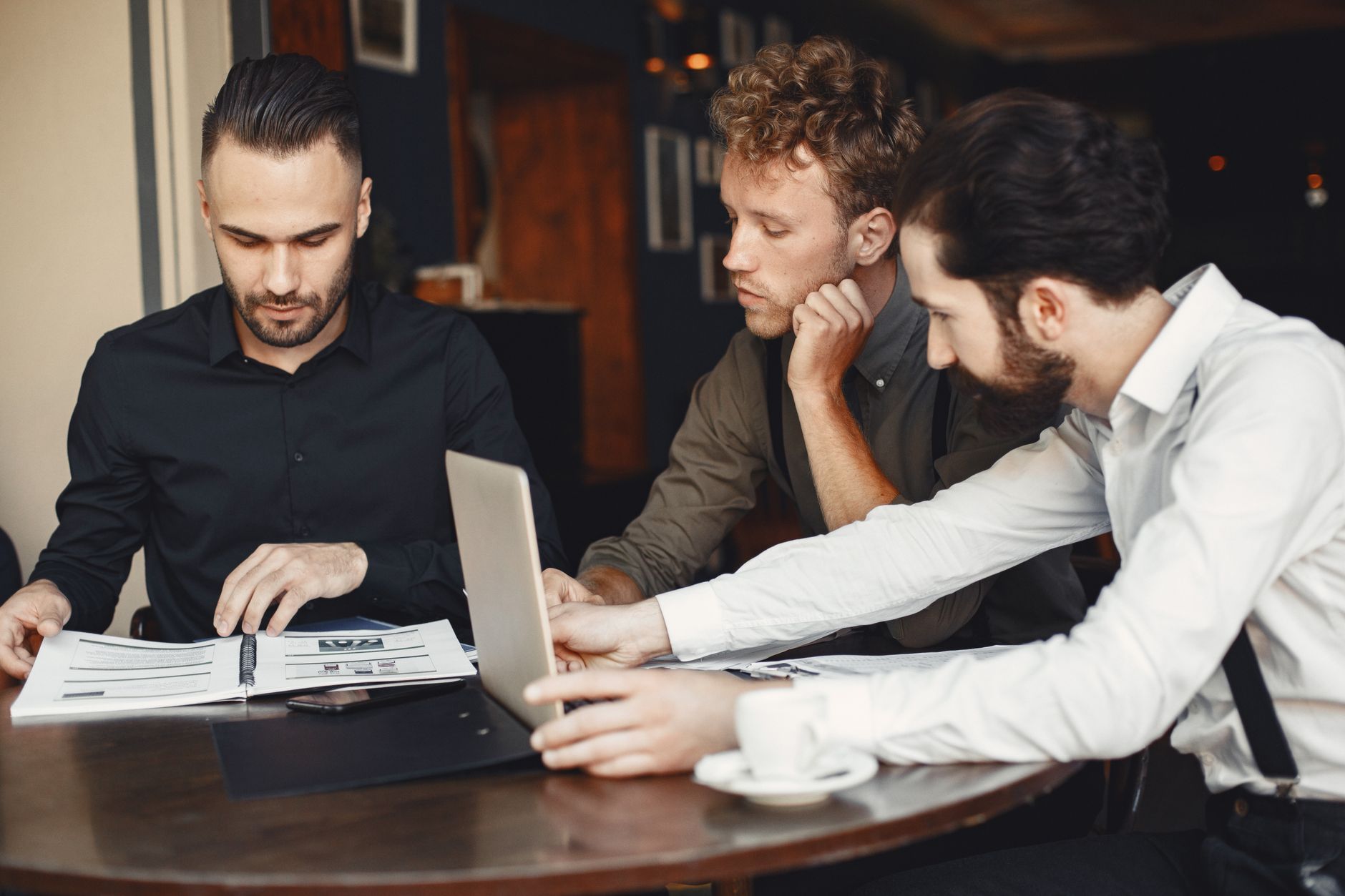 Three men collaborate over documents and a laptop during a business meeting.