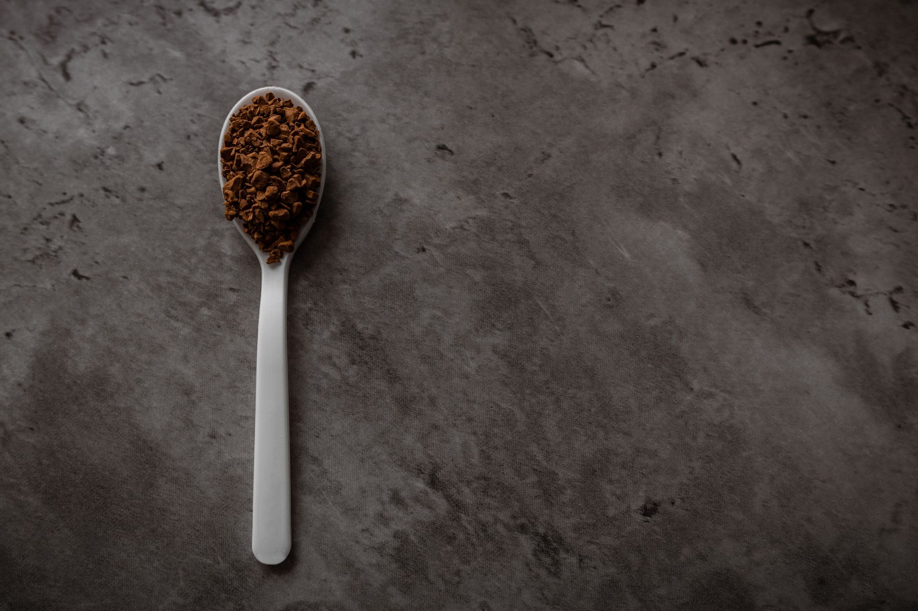 A spoon filled with instant coffee on a dark textured background, perfect for beverage themes.