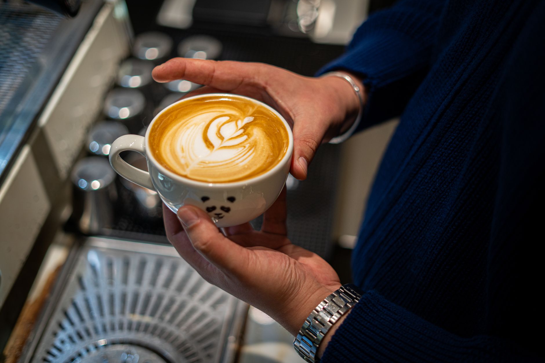 Barista holding a cup of latte with beautiful leaf pattern art, showcasing craftsmanship.