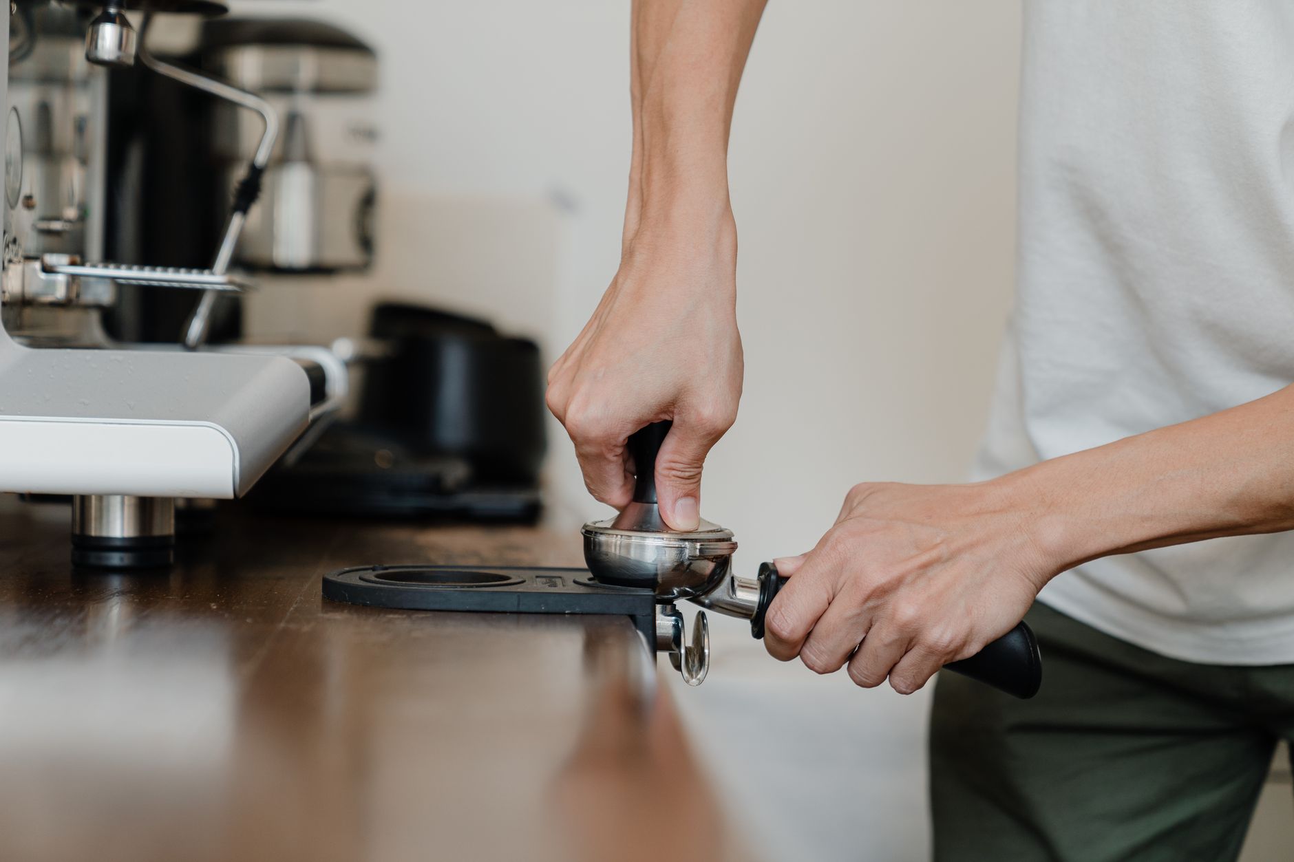 Unrecognizable person pressuring ground coffee in portafilter with tamper while preparing delicious aromatic espresso during work in coffee shop