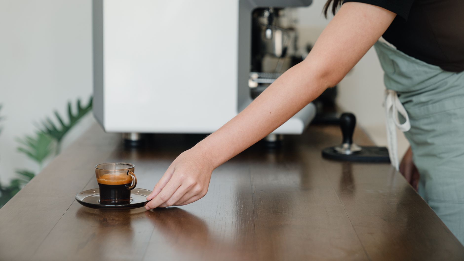 Crop unrecognizable female barista in apron serving freshly brewed aromatic coffee in stylish cup and saucer while working in modern coffee shop