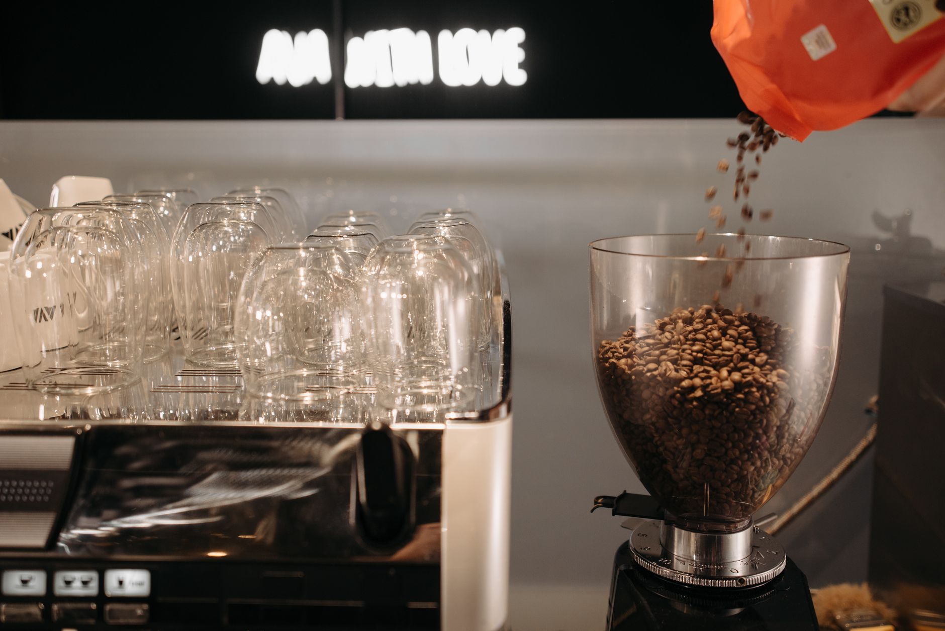 High-quality image of coffee beans being poured into a grinder next to a stacked set of glasses, perfect for cafe or barista themes.
