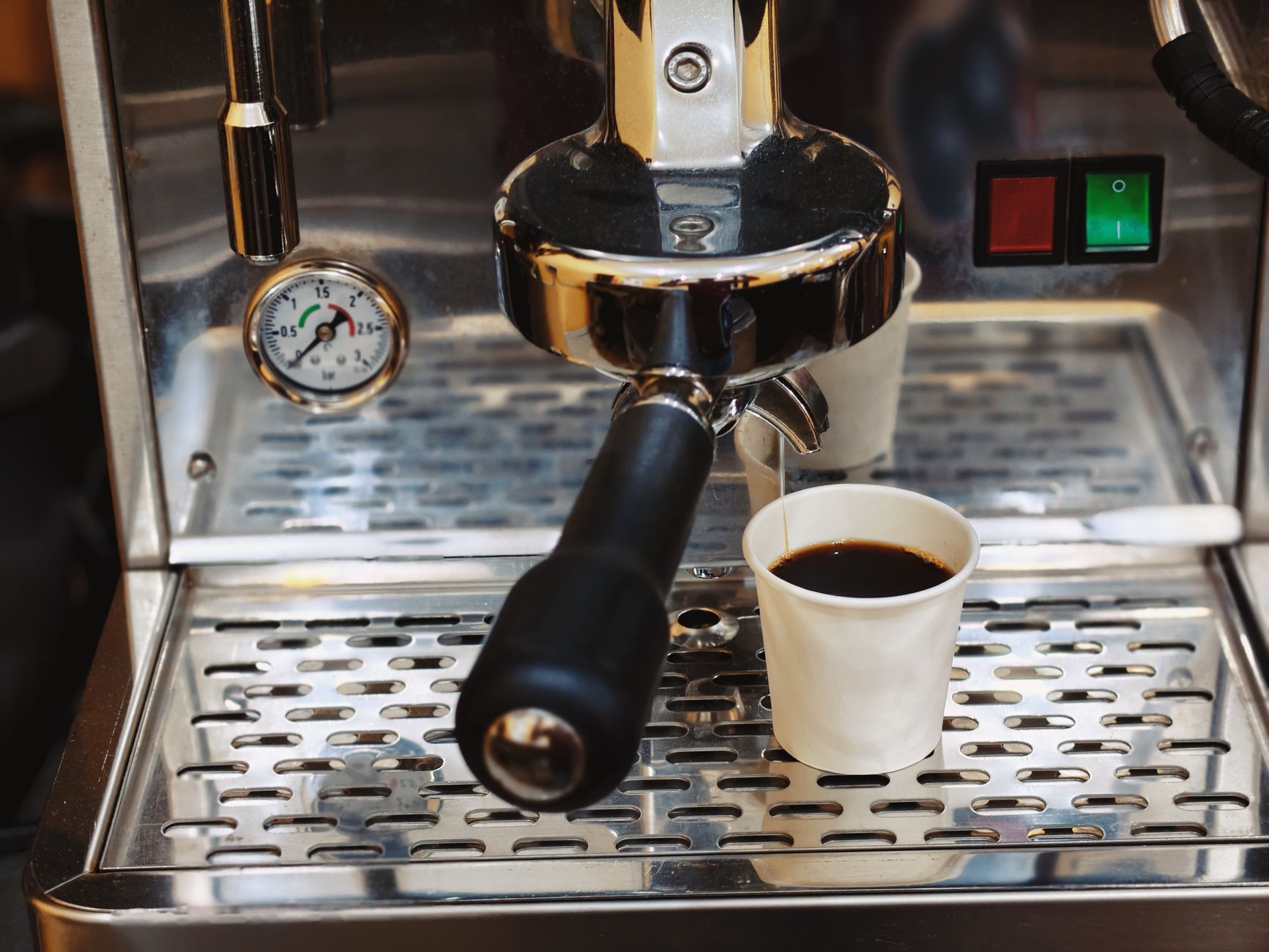 Close-up of an espresso machine brewing coffee into a paper cup.