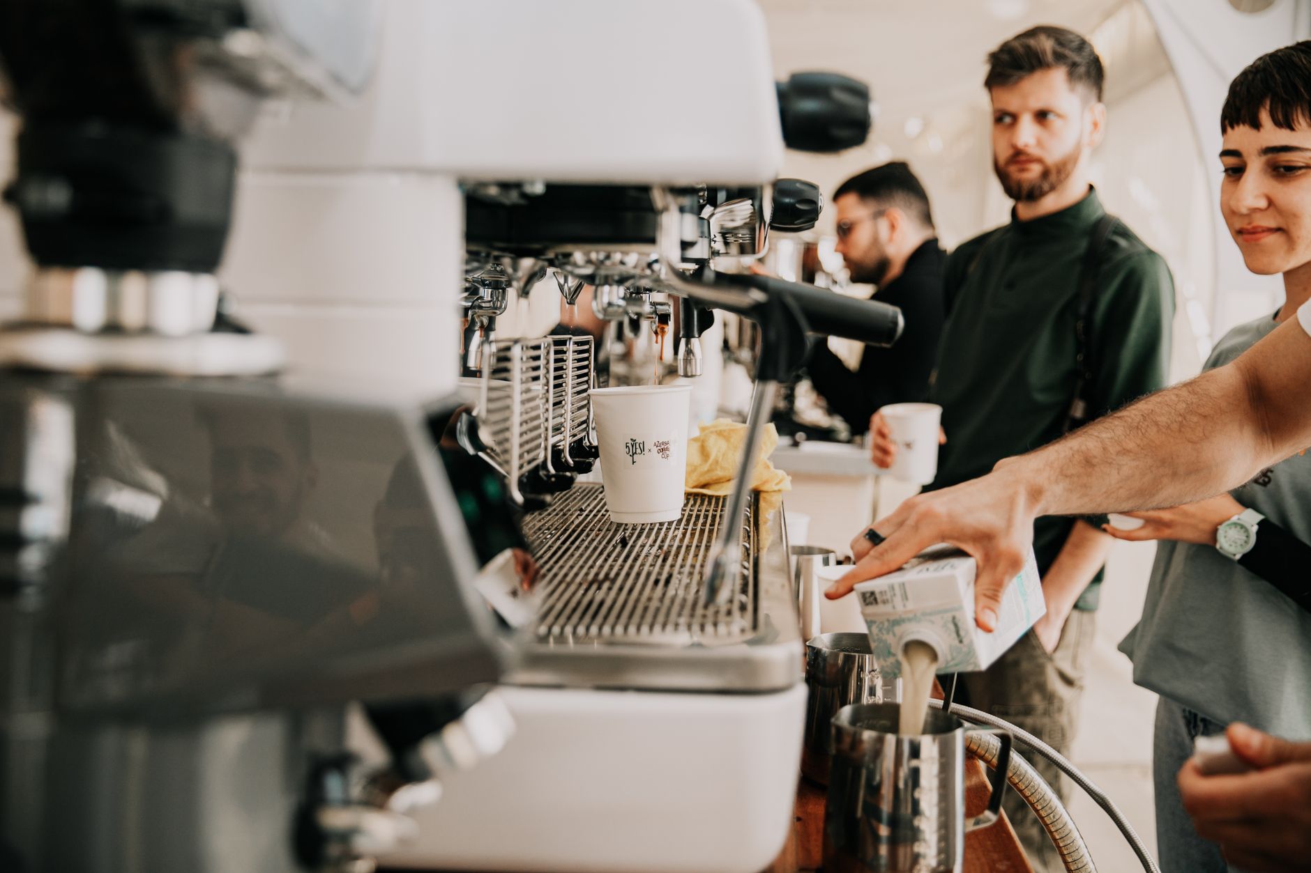 A barista prepares coffee in a bustling café, engaging with customers and creating vibrant, welcoming vibes.