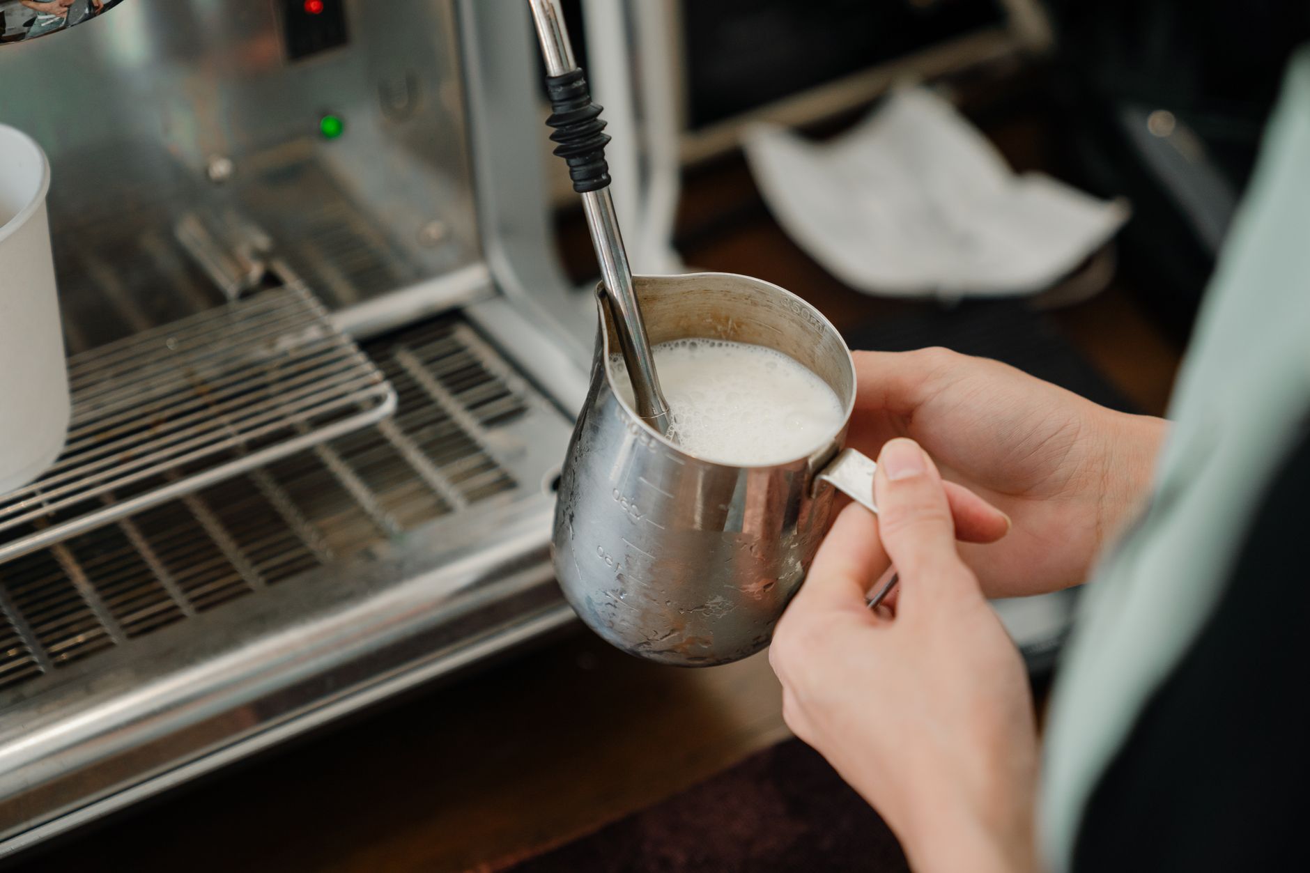 Crop unrecognizable coffee shop worker whipping fresh milk in pitcher using coffee machine while preparing hot coffee in cafe