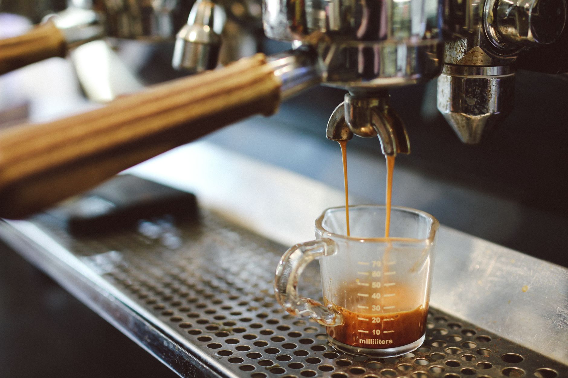 Professional coffee machine preparing fresh espresso and pouring into glass cup in daytime