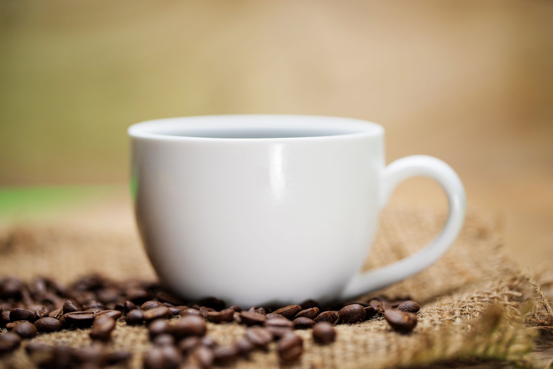 White coffee cup resting on burlap with scattered coffee beans in warm lighting.