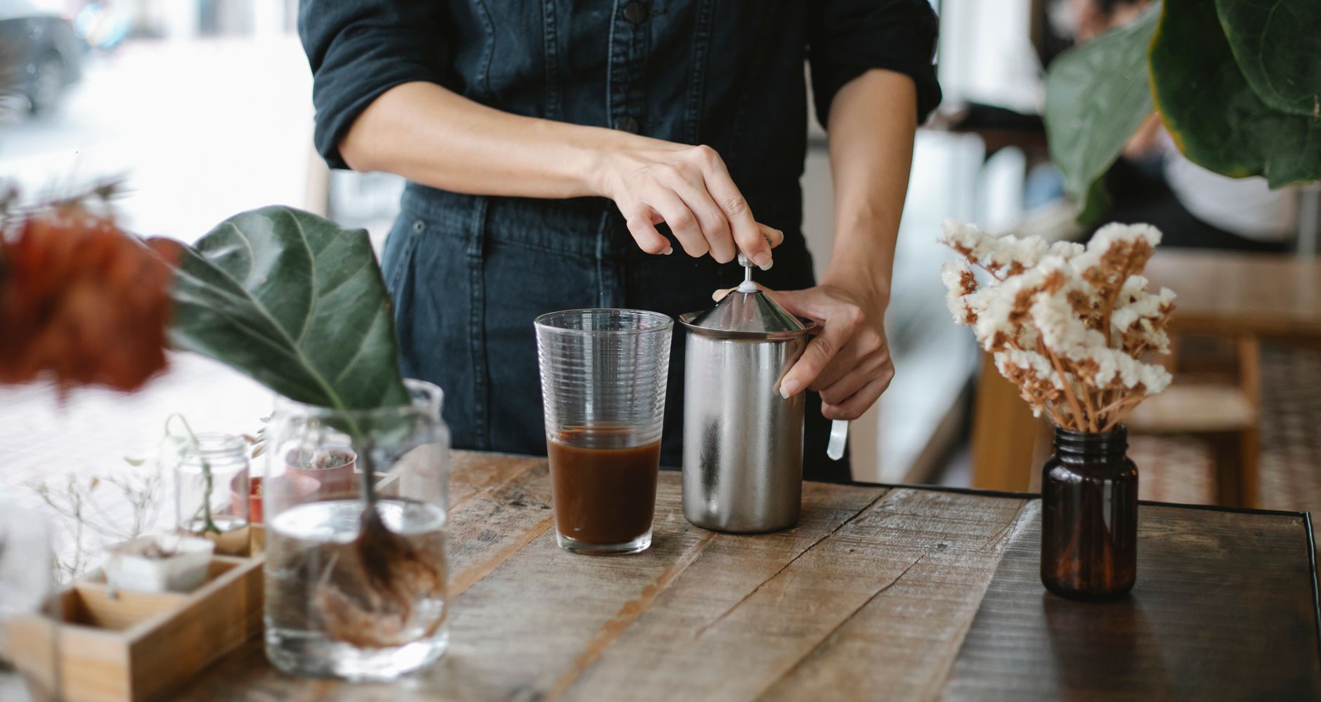 Crop anonymous female barista opening manual milk frother lid while preparing iced chocolate coffee in cafeteria