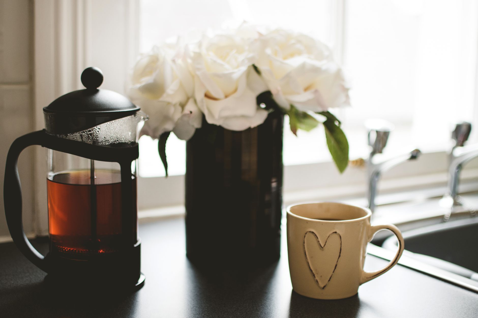 A serene morning setting with a French press coffee and white roses by the kitchen window.
