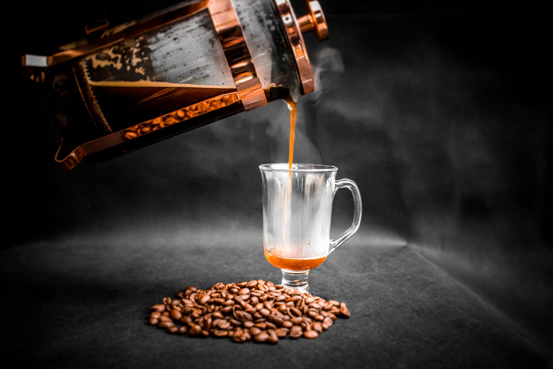 Aromatic hot coffee being poured from French press into elegant glass with pile of coffee beans beside on black background