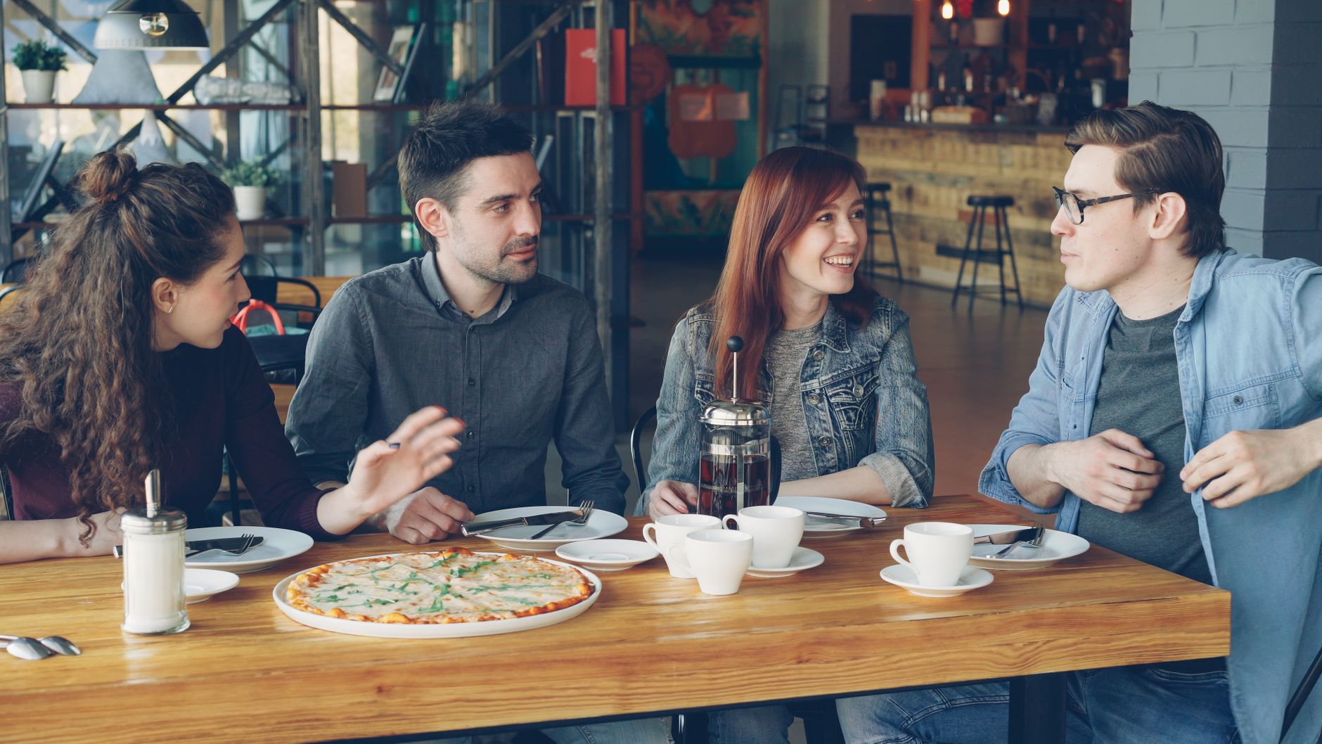 A group of adults enjoying coffee and pizza in a modern café atmosphere.