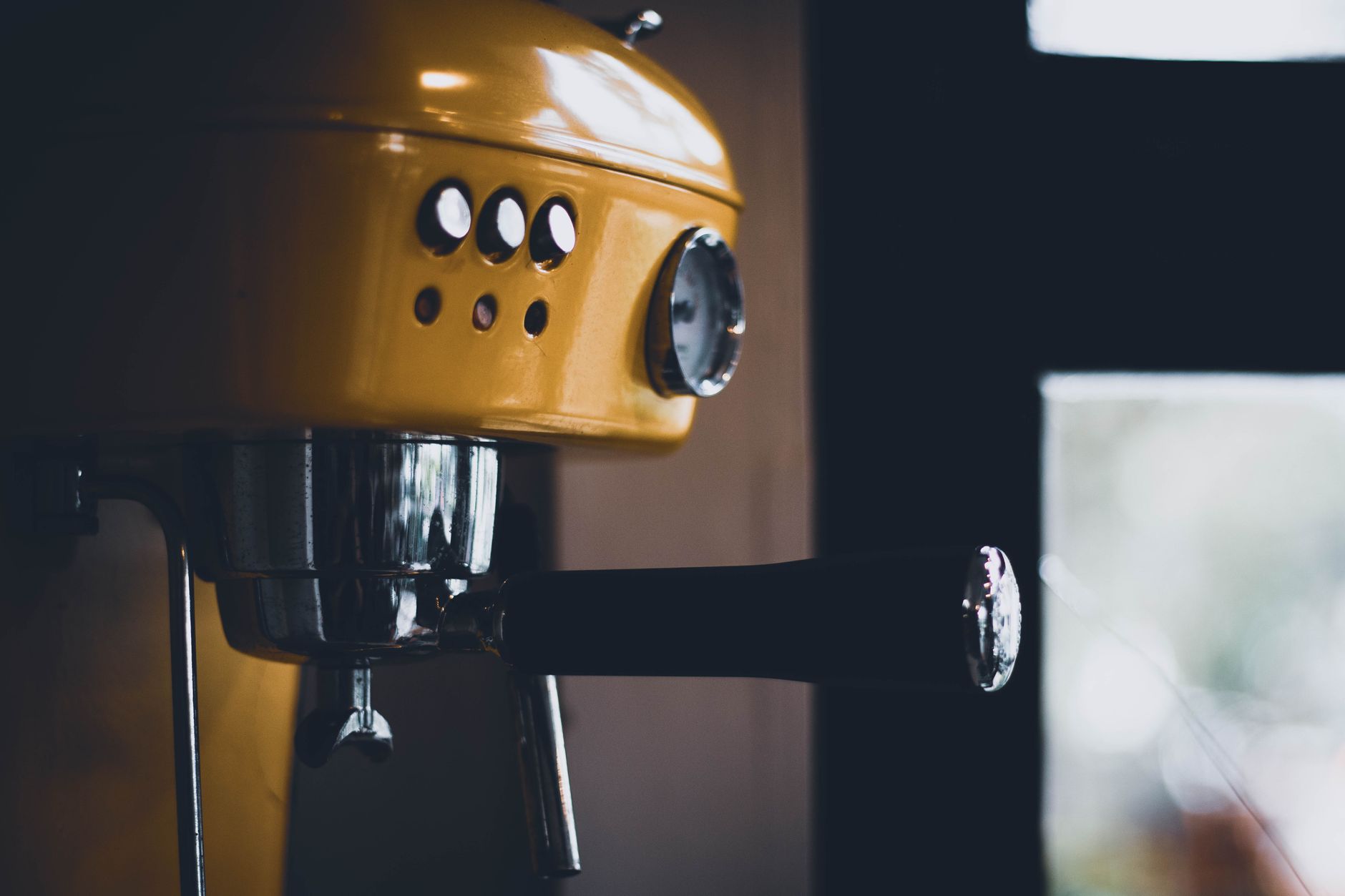 Close-up of a yellow espresso machine in a dimly lit kitchen setting, highlighting its vintage style.