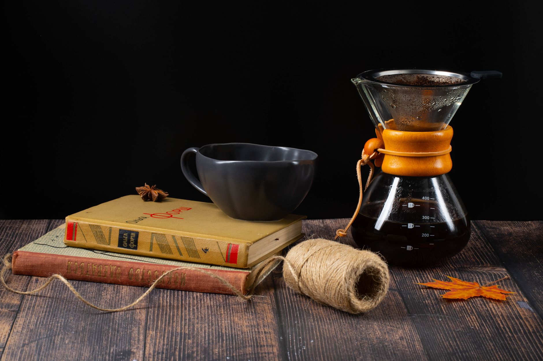 A cozy fall scene featuring a coffee setup with books, a mug, and a Chemex on a wooden table.