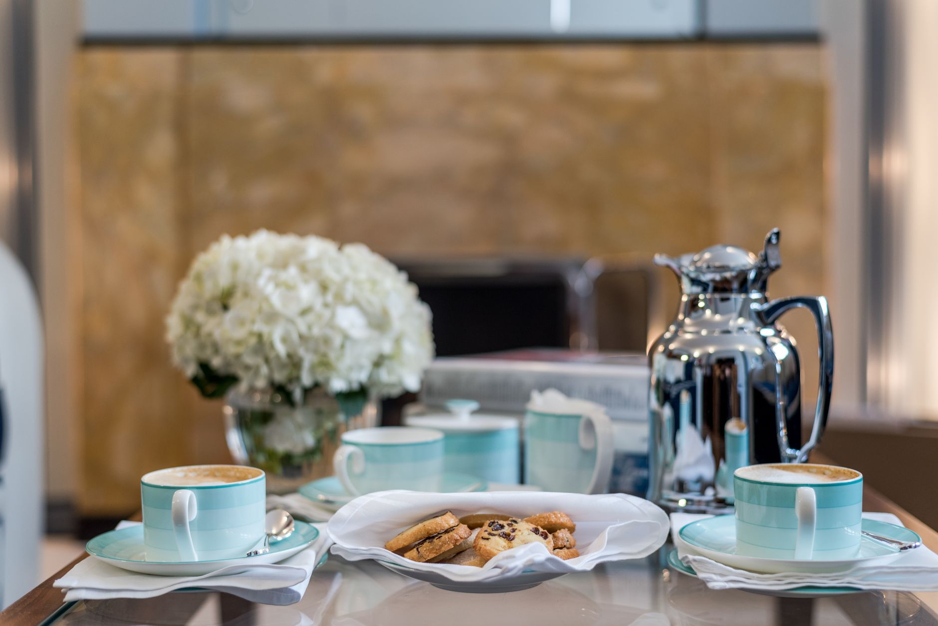 A stylish breakfast setup with coffee cups, cookies, and flowers on a table.