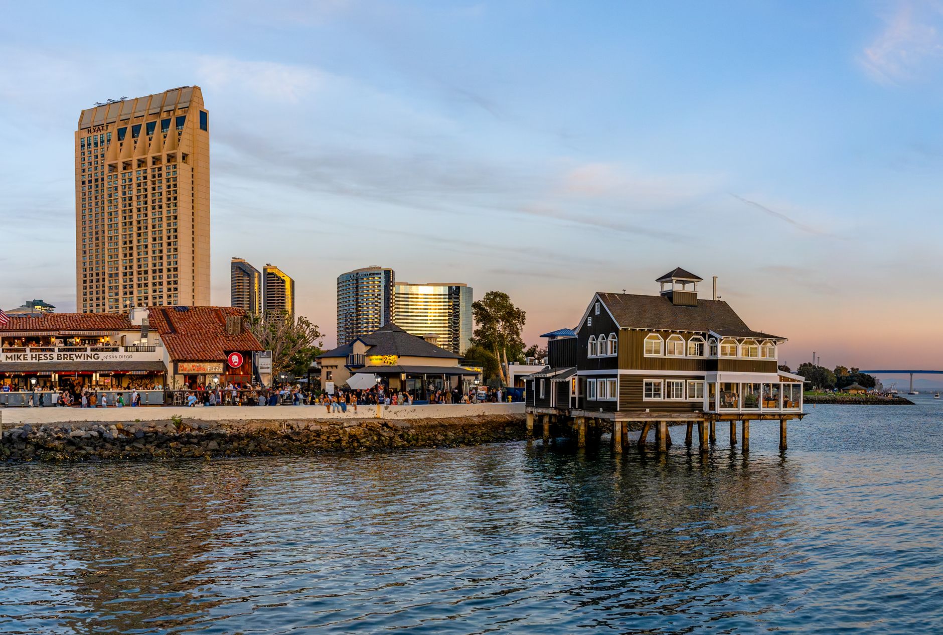 Scenic view of San Diego Bay's waterfront showcasing iconic buildings and restaurants at sunset.
