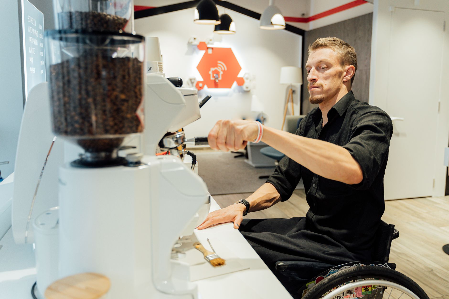Barista in a wheelchair operating an espresso machine in a modern coffee shop setting.