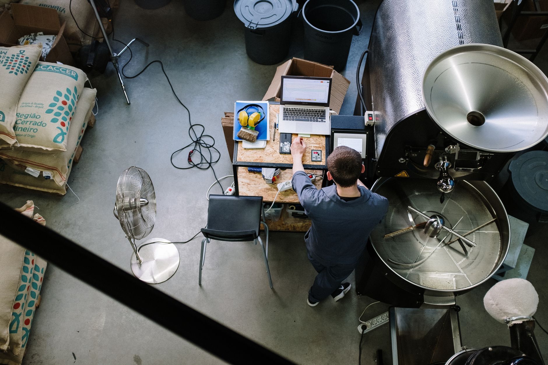 Overhead view of a coffee roaster operating machinery in an industrial environment.