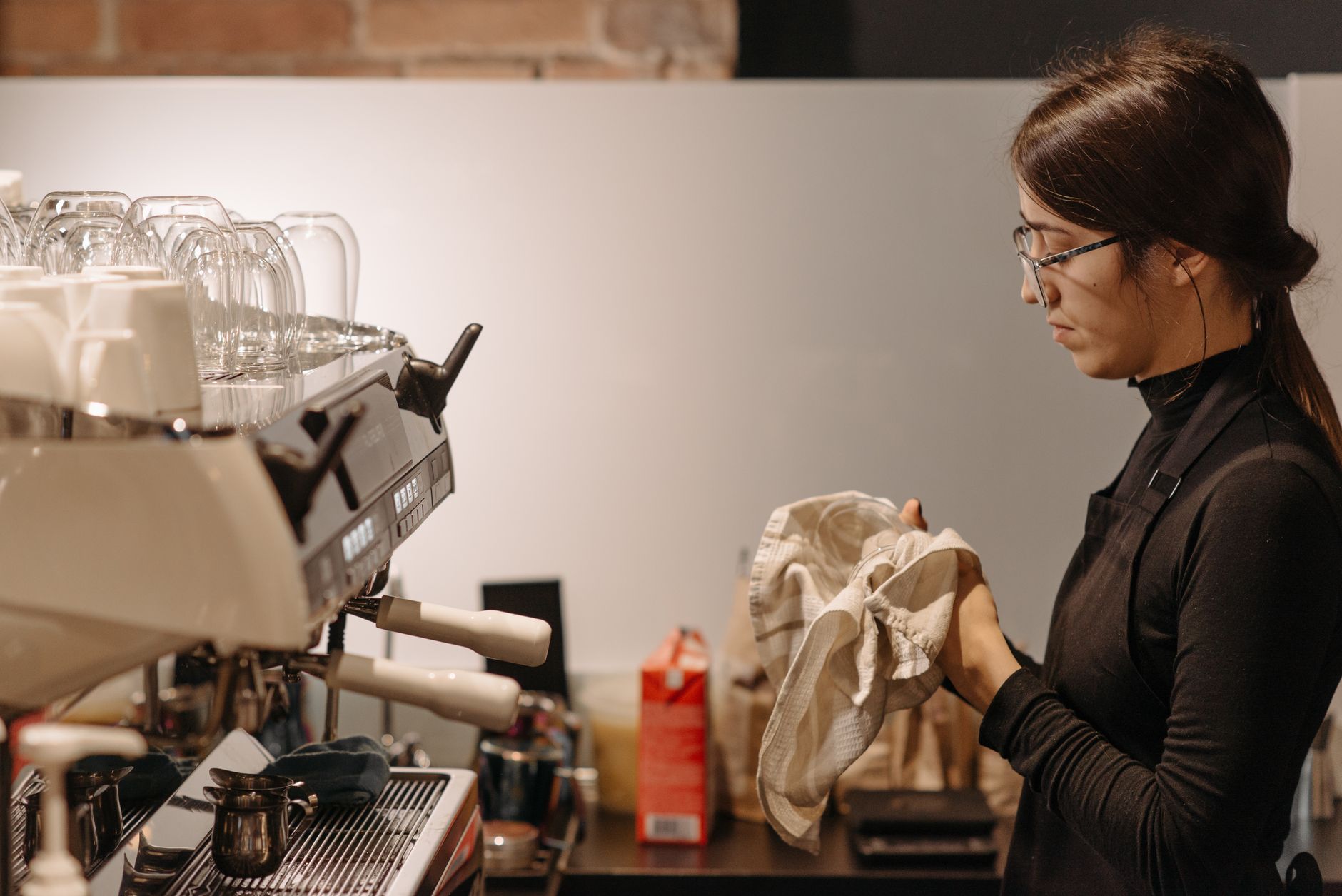 Barista cleaning utensils at a coffee machine inside a cafe.