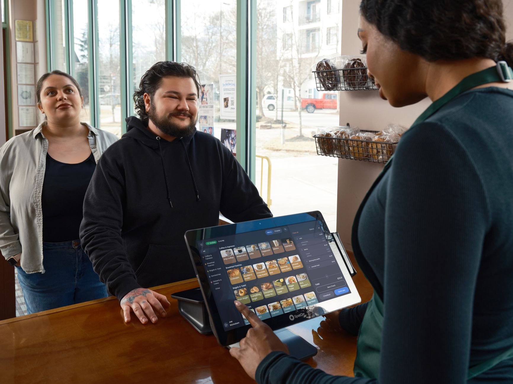 Barista using POS system to serve two customers at a café counter, showcasing modern restaurant technology.