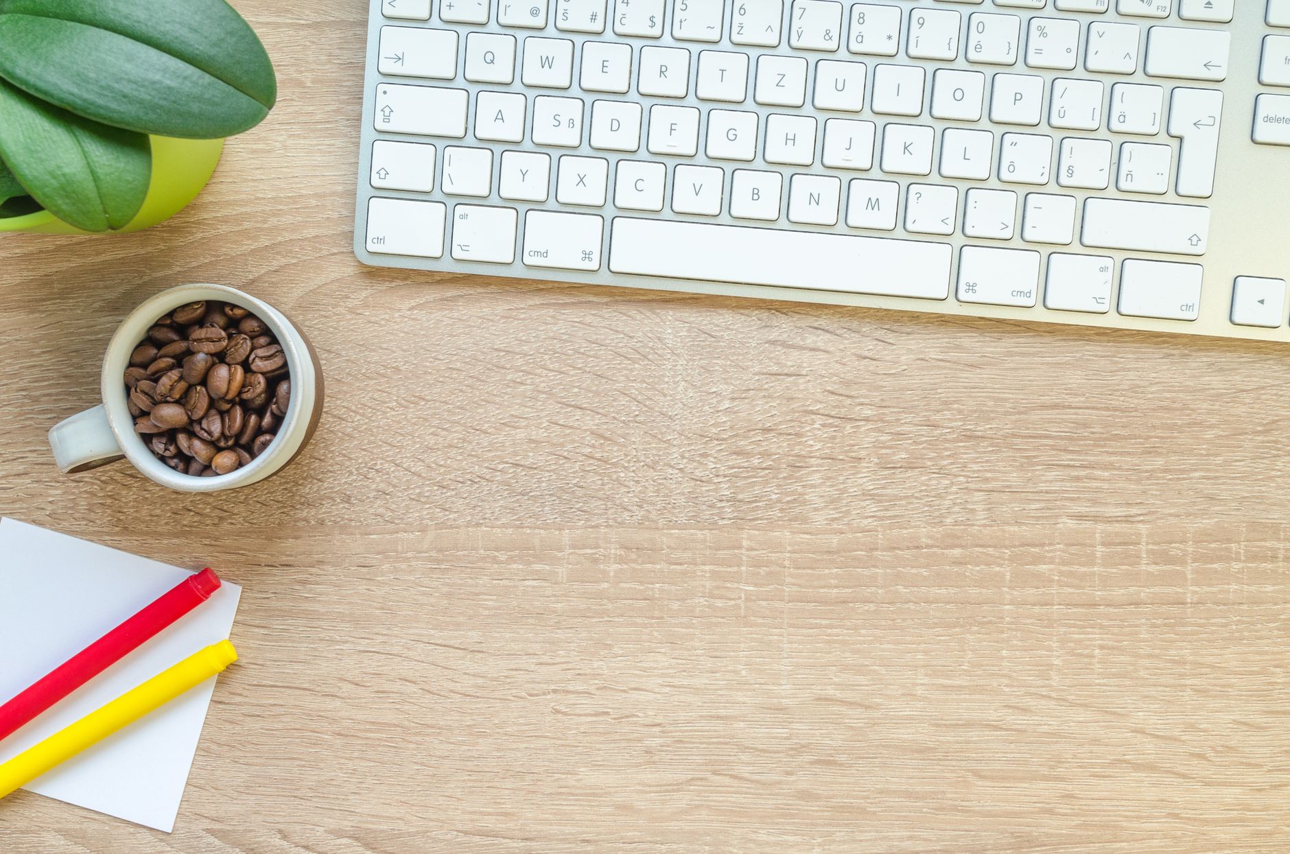 Overhead view of keyboard, coffee beans, and stationery on a wooden desk.