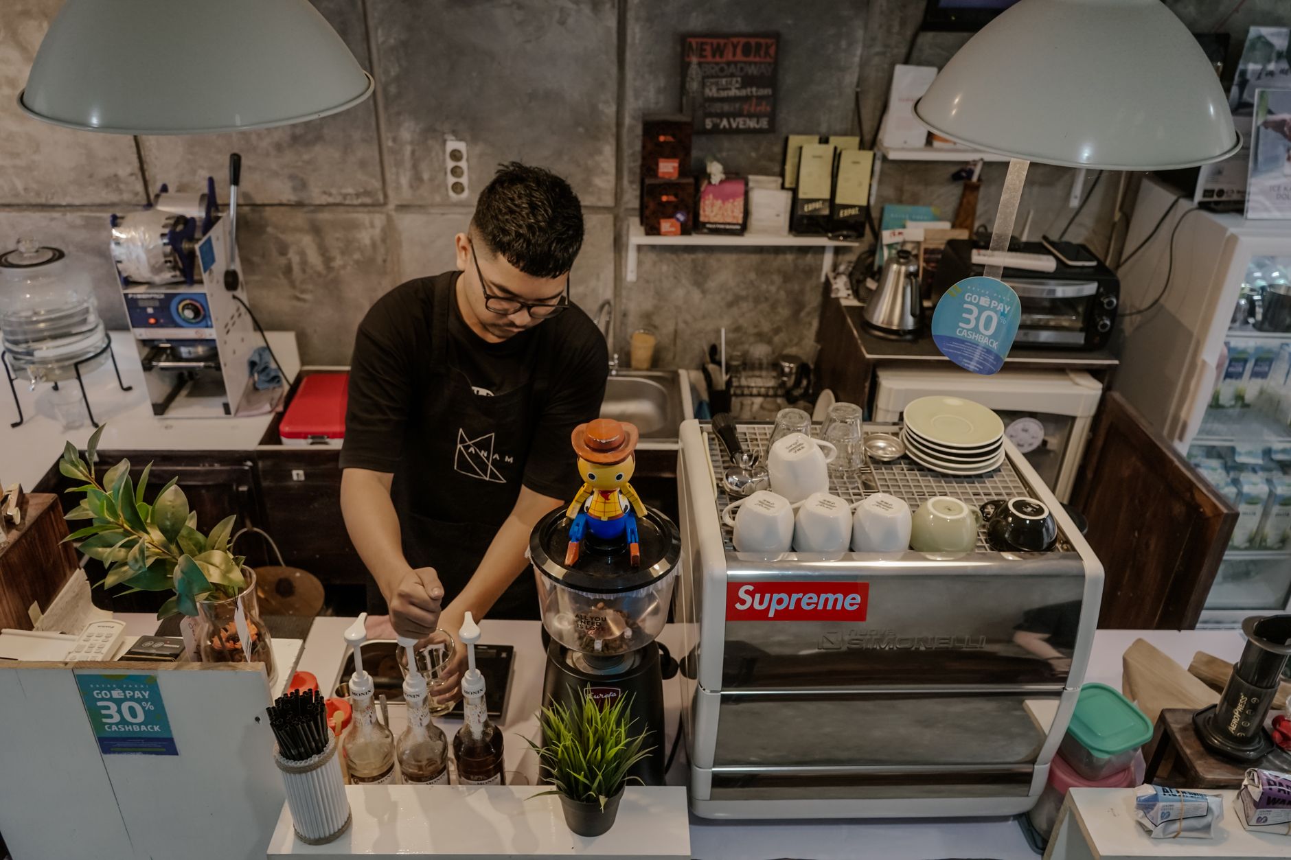 From above of serious bearded ethnic male barista in casual wear and eyeglasses working in cafeteria