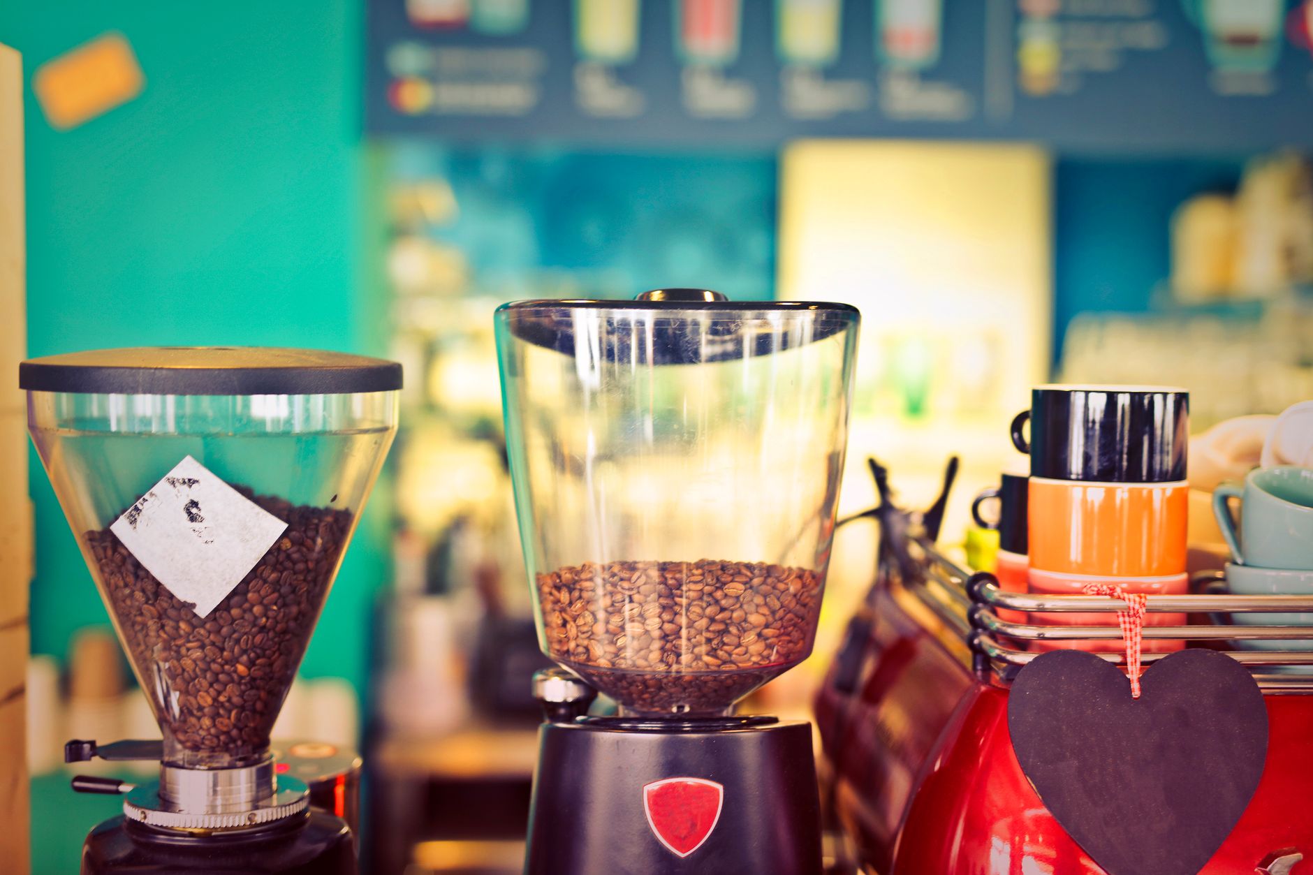 Close-up of coffee grinders and cups in a colorful cafe setting.