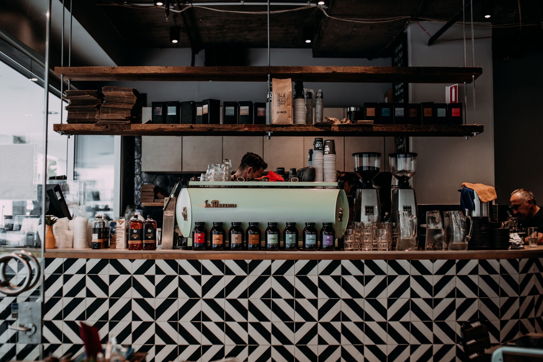 Modern coffee shop interior featuring a stylish counter with geometric patterns and shelves with cups and coffee bags.