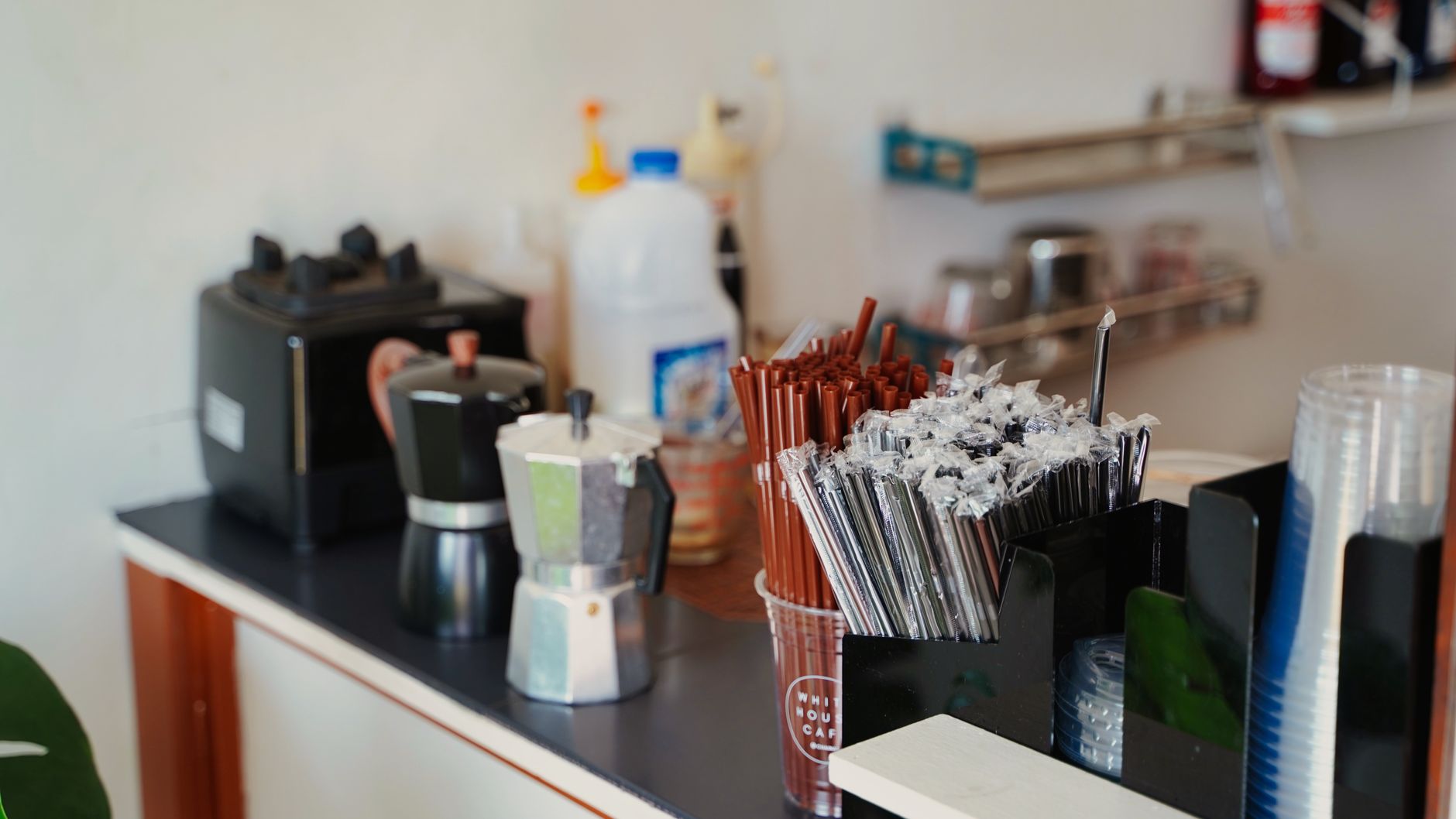 A coffee shop counter with barista tools and supplies, including moka pots and straws.