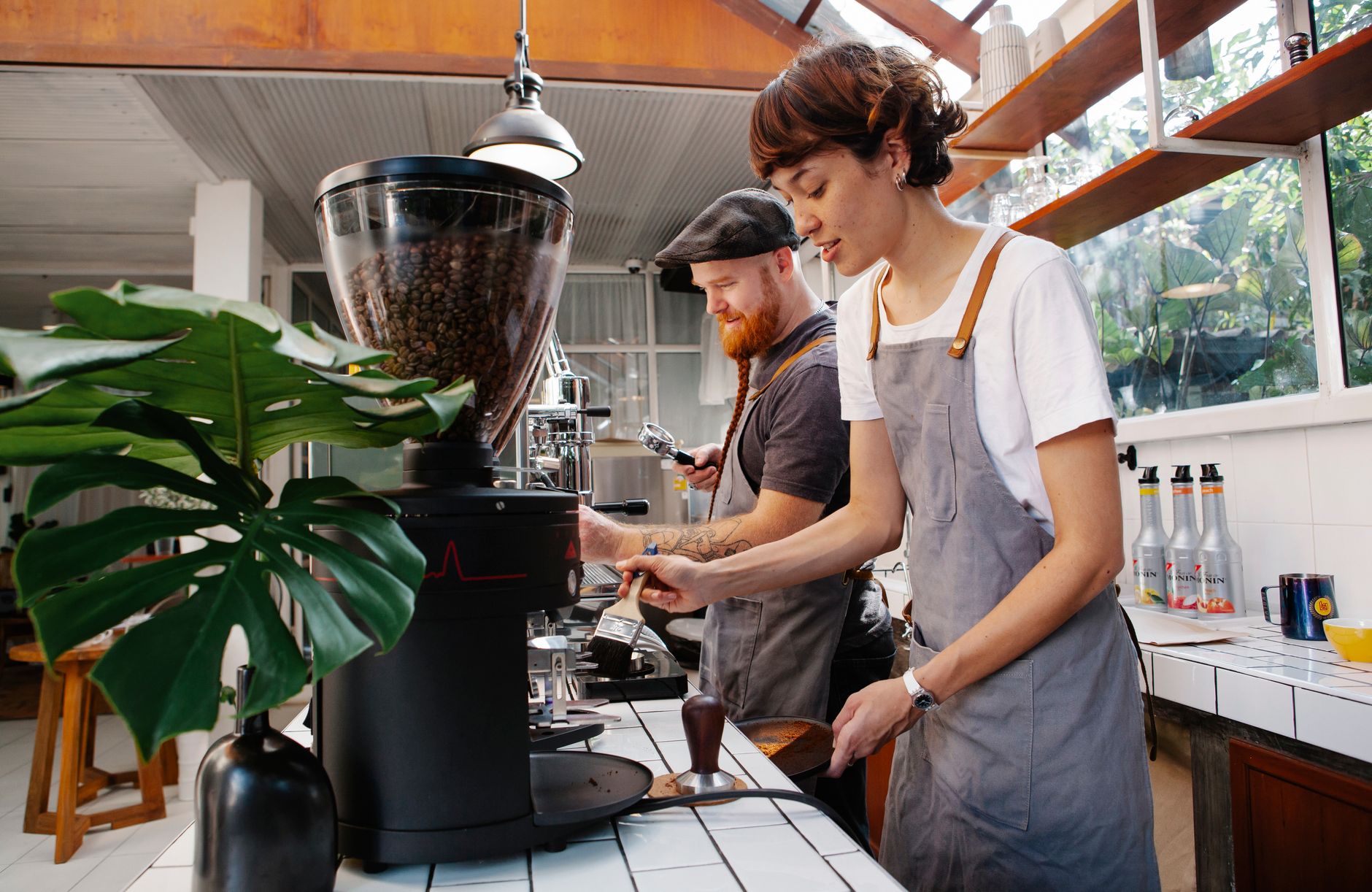 Side view of young female employee with hipster male coworker preparing hot drinks in coffee makers in cafeteria