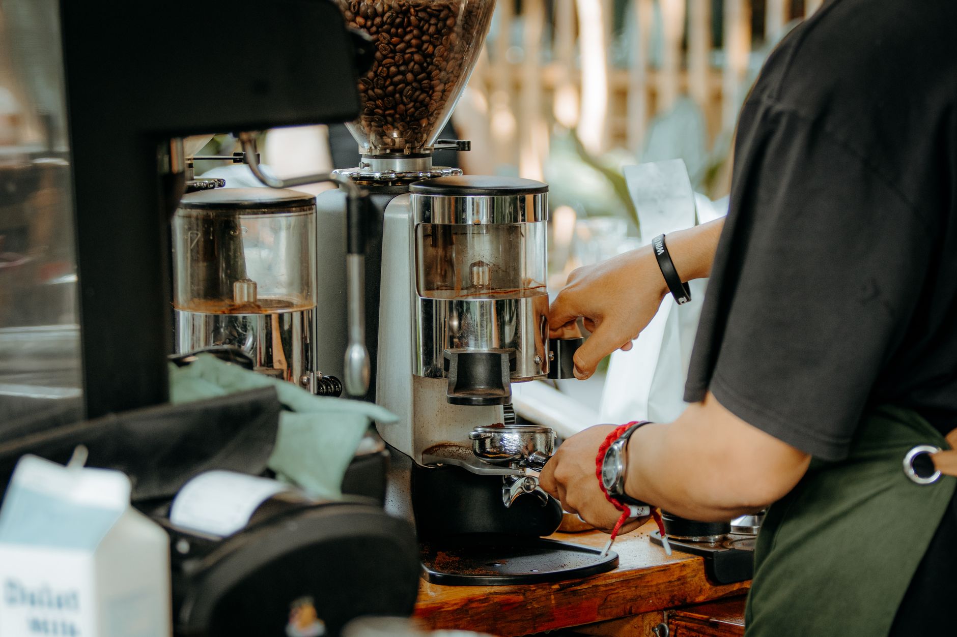 Barista using a coffee grinder to prepare espresso in a modern cafe setting.