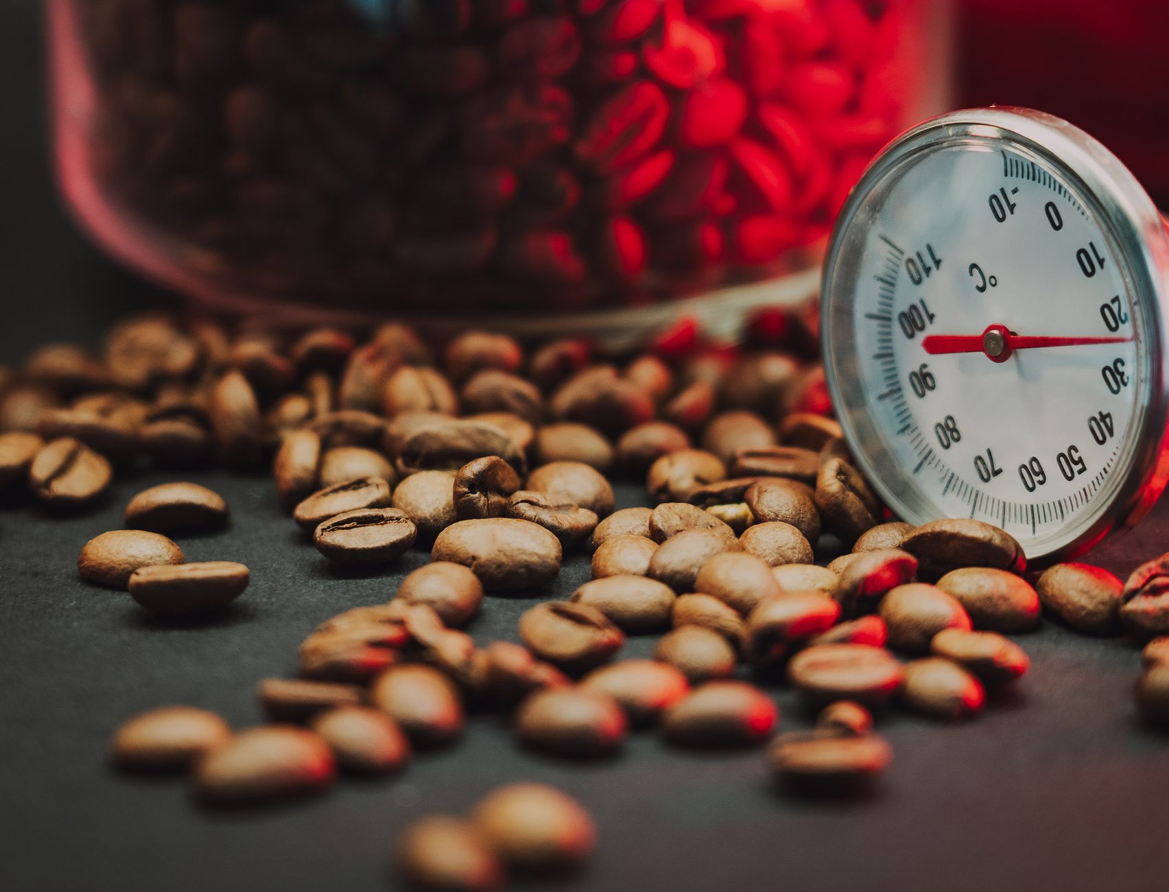 Coffee beans scattered on a table with a thermometer, highlighting precision in coffee-making.