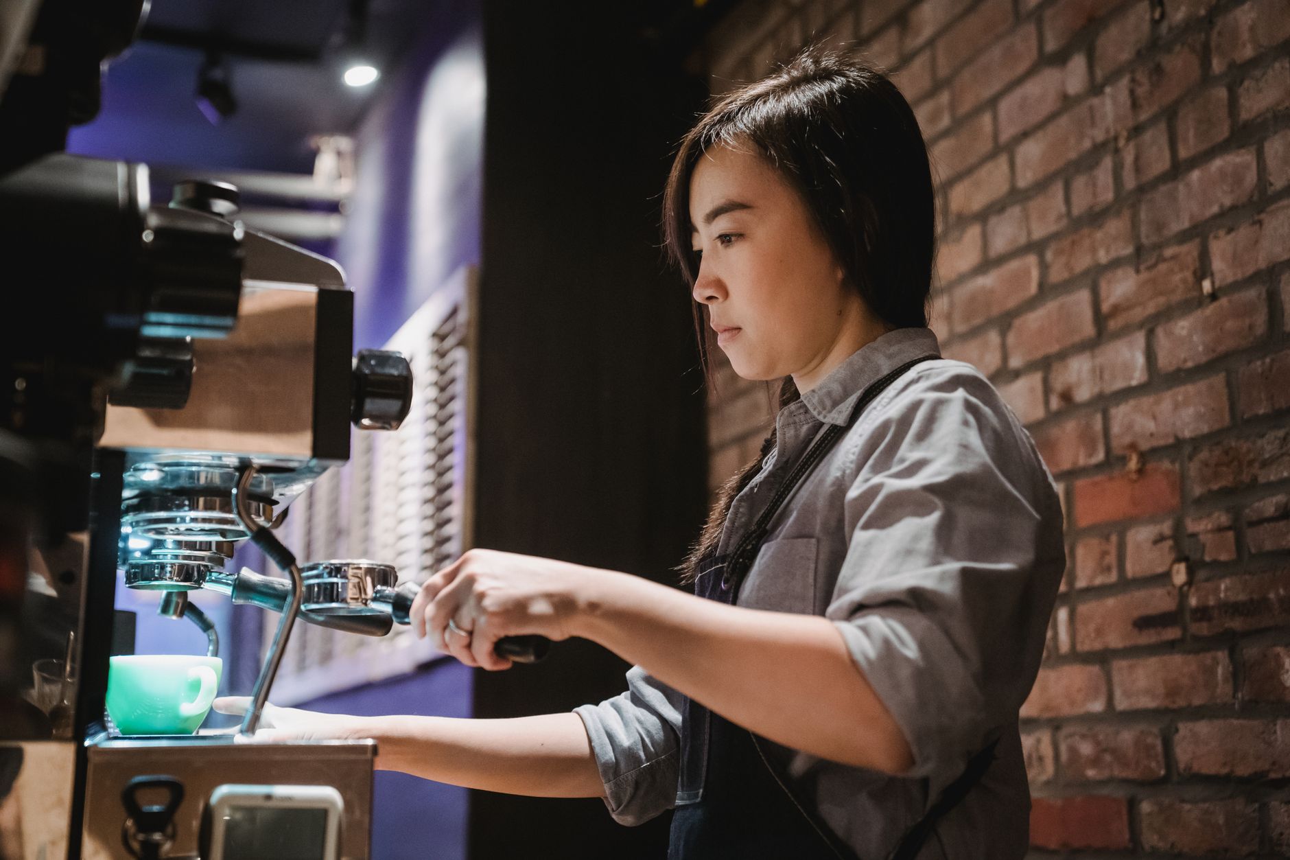 A barista skillfully operates a coffee machine, emphasizing dedication and expertise in a cozy café setting.