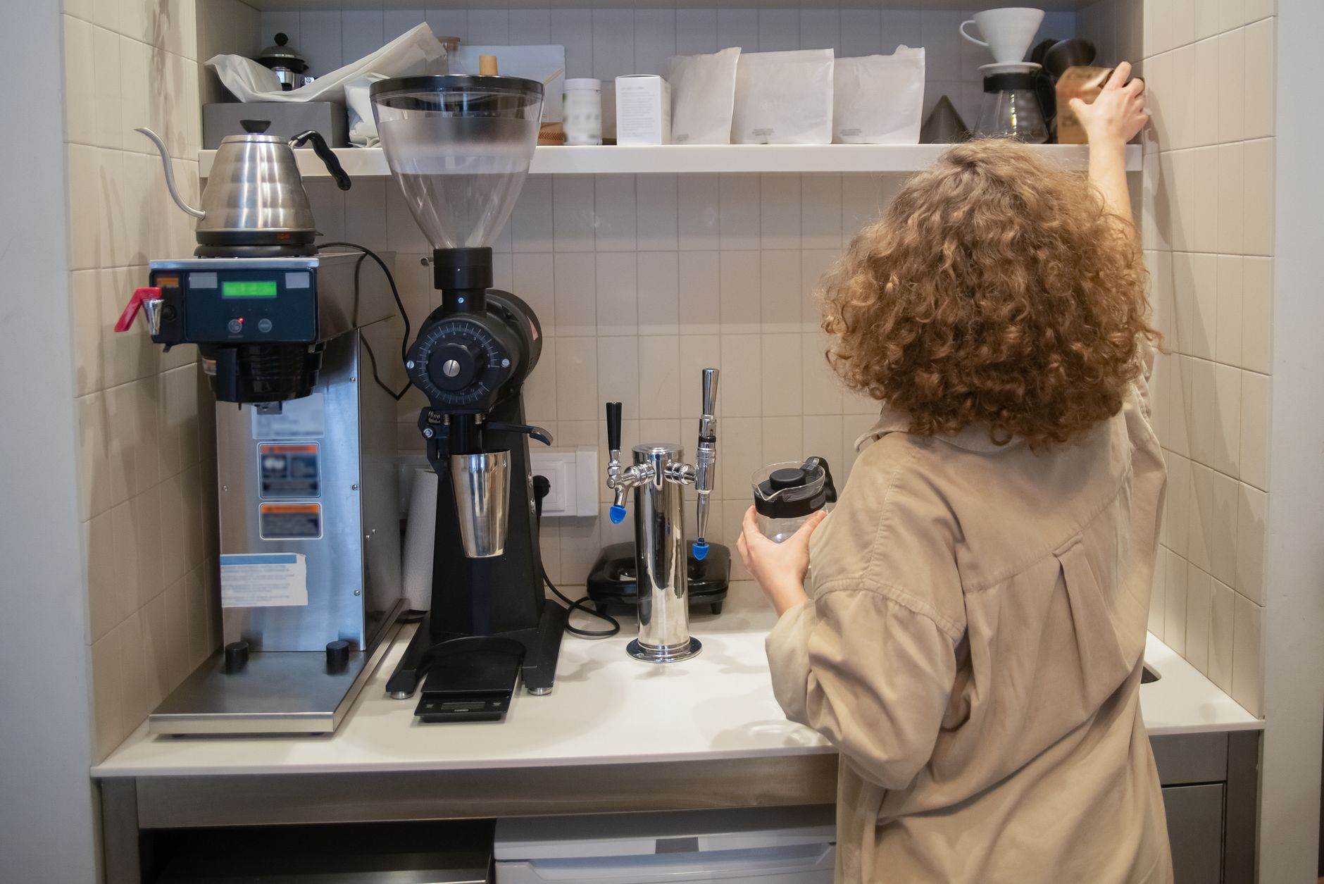 A woman is reaching for coffee-making equipment in a modern kitchen setting, showcasing barista skills.