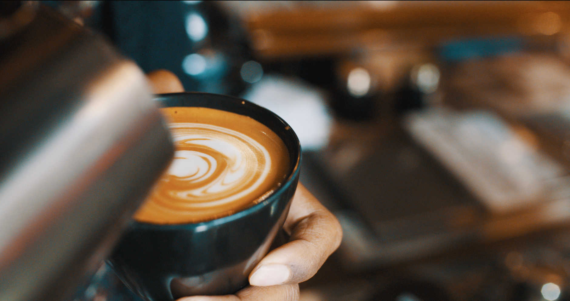 Close-up of a barista pouring a latte with artistic foam design in a cozy coffee shop.