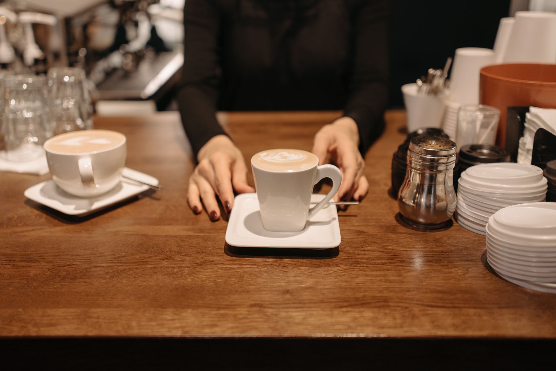 Barista hands serving cappuccinos with latte art on wooden counter in a cozy cafe.