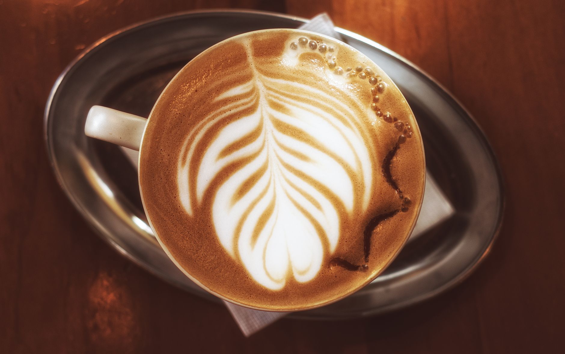 A top view of a latte with intricate art served in a ceramic cup on a metallic tray.