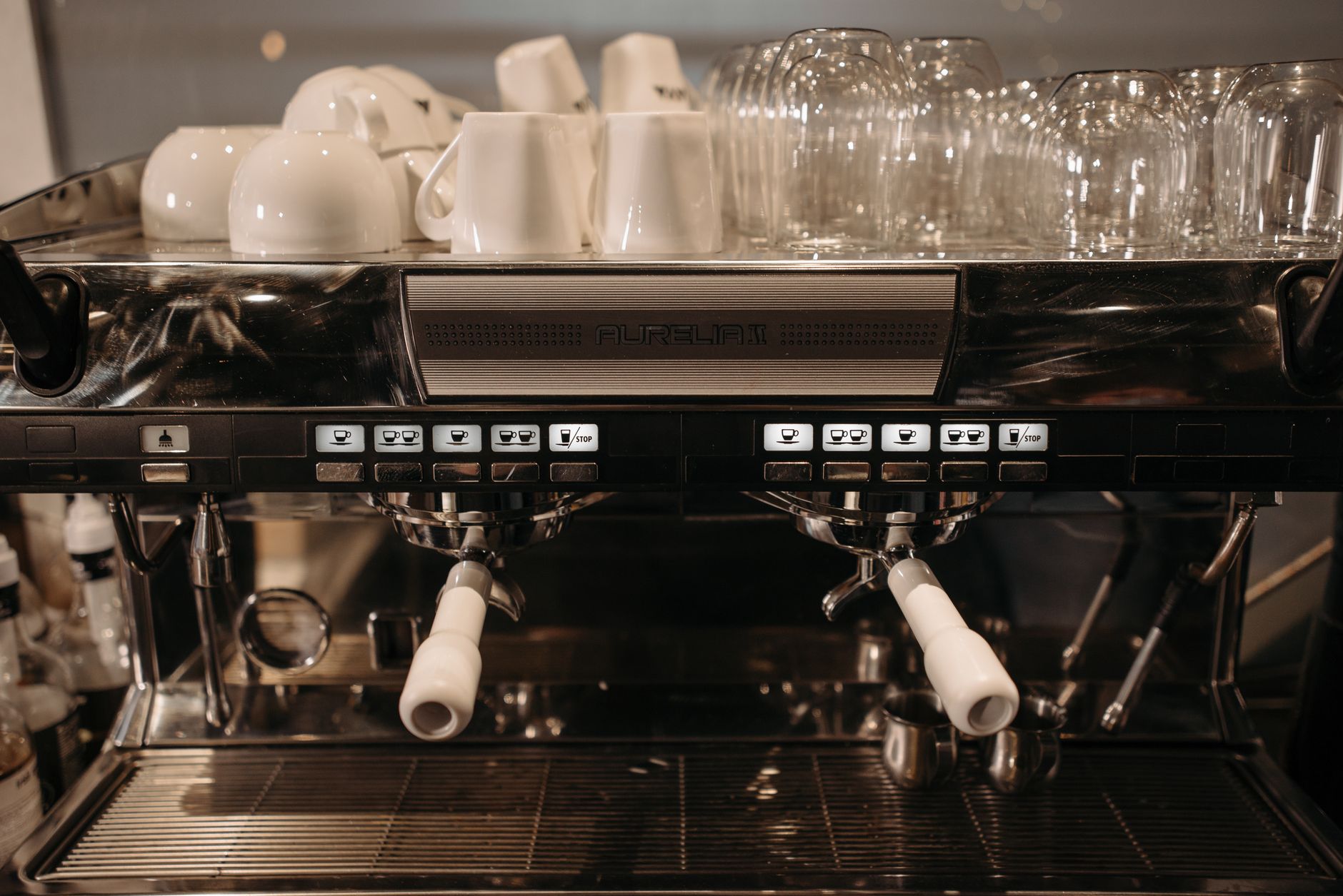 Close-up of a commercial espresso machine with cups and glasses stacked on top, ready for coffee brewing.