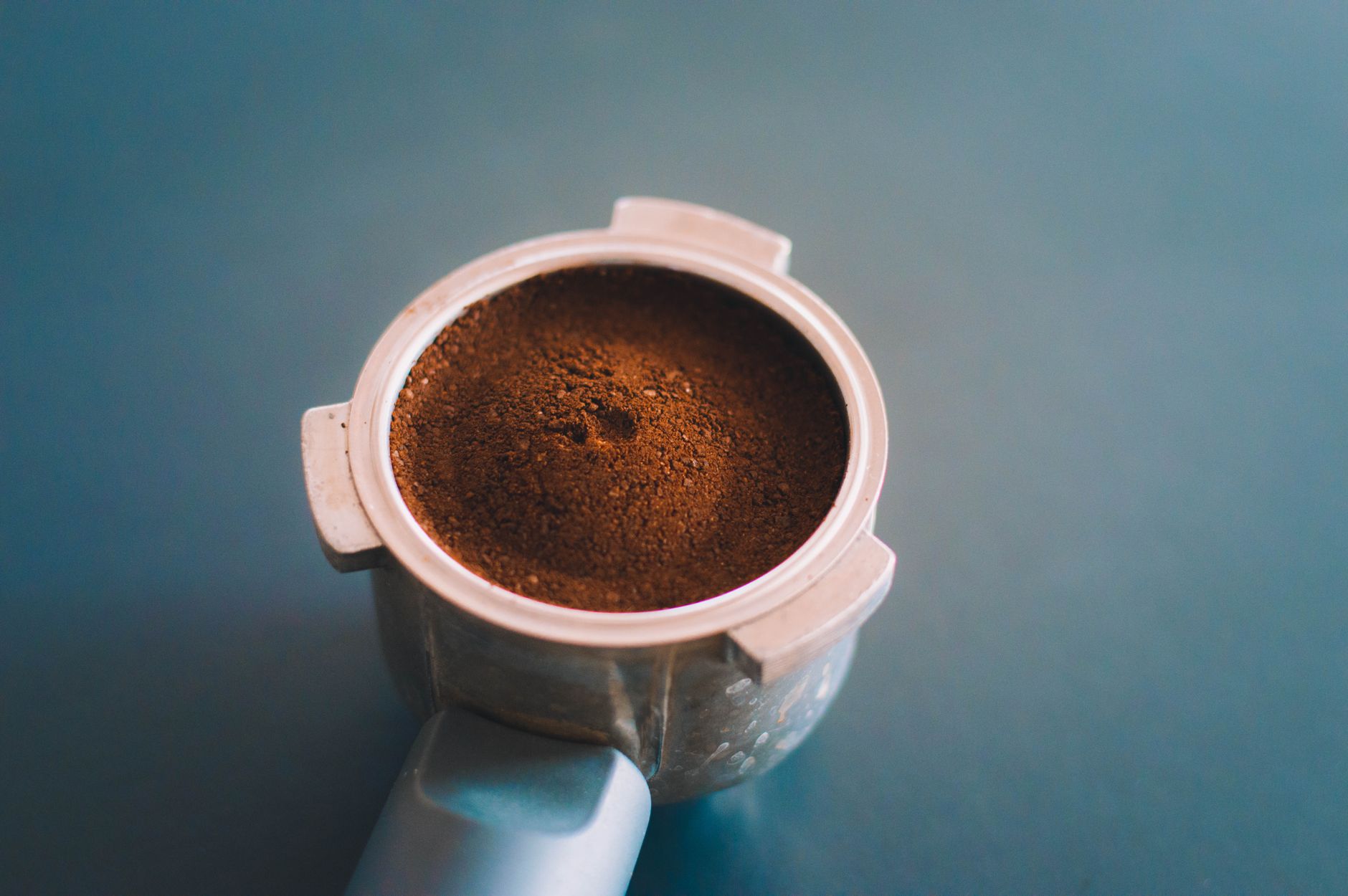 A detailed view of freshly ground coffee in a portafilter against a blue background.