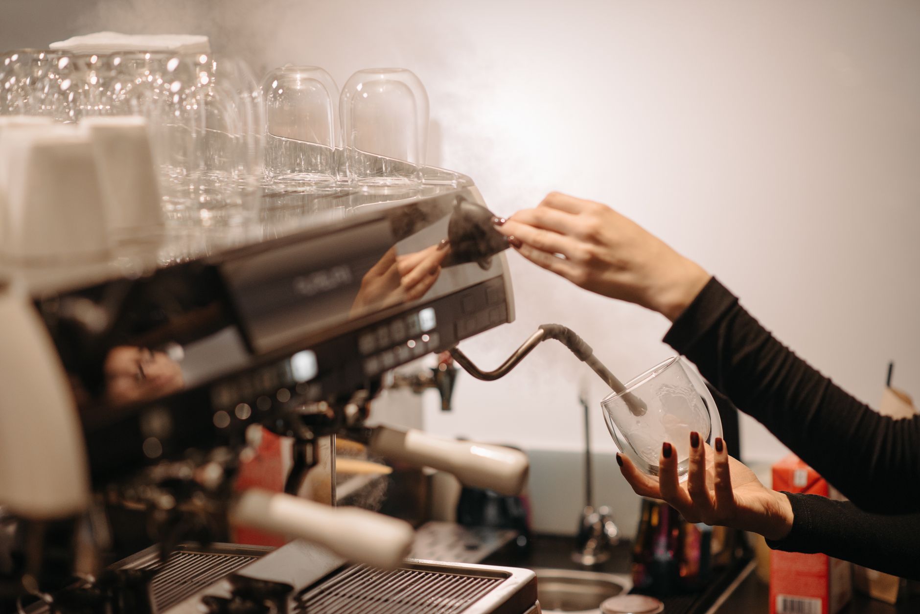 Close-up of a barista steaming milk using an espresso machine in a coffee shop.