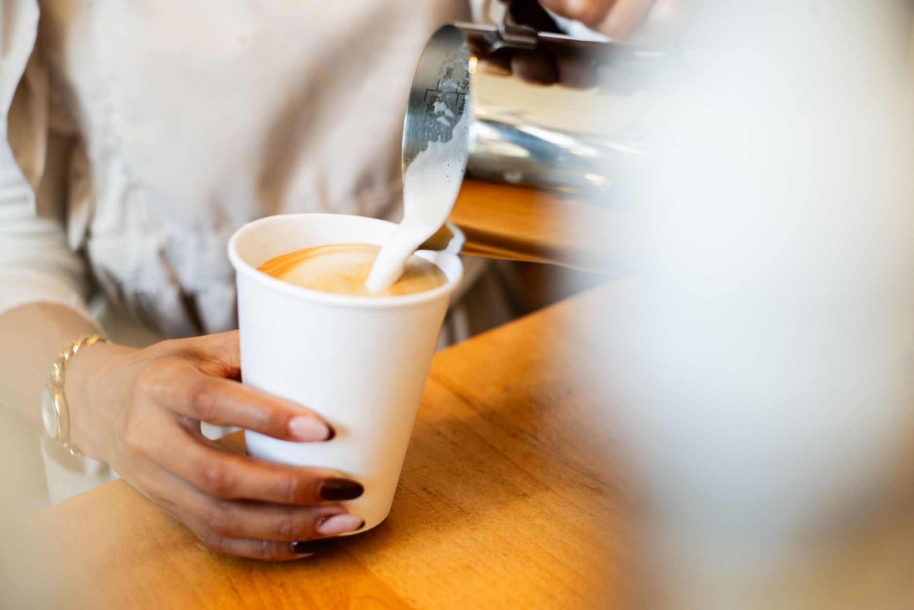 A close-up of a barista pouring milk into a coffee cup, showcasing barista skills.
