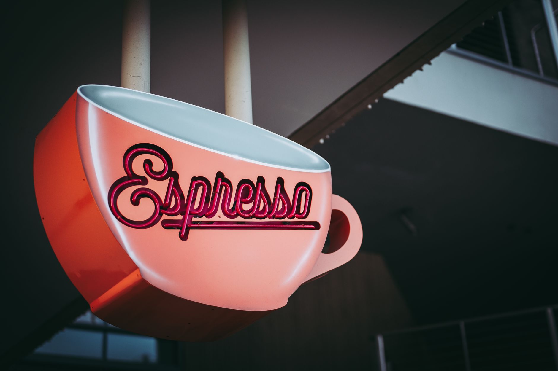 Neon sign in the shape of an espresso cup, creating a retro ambiance outside a coffee shop.